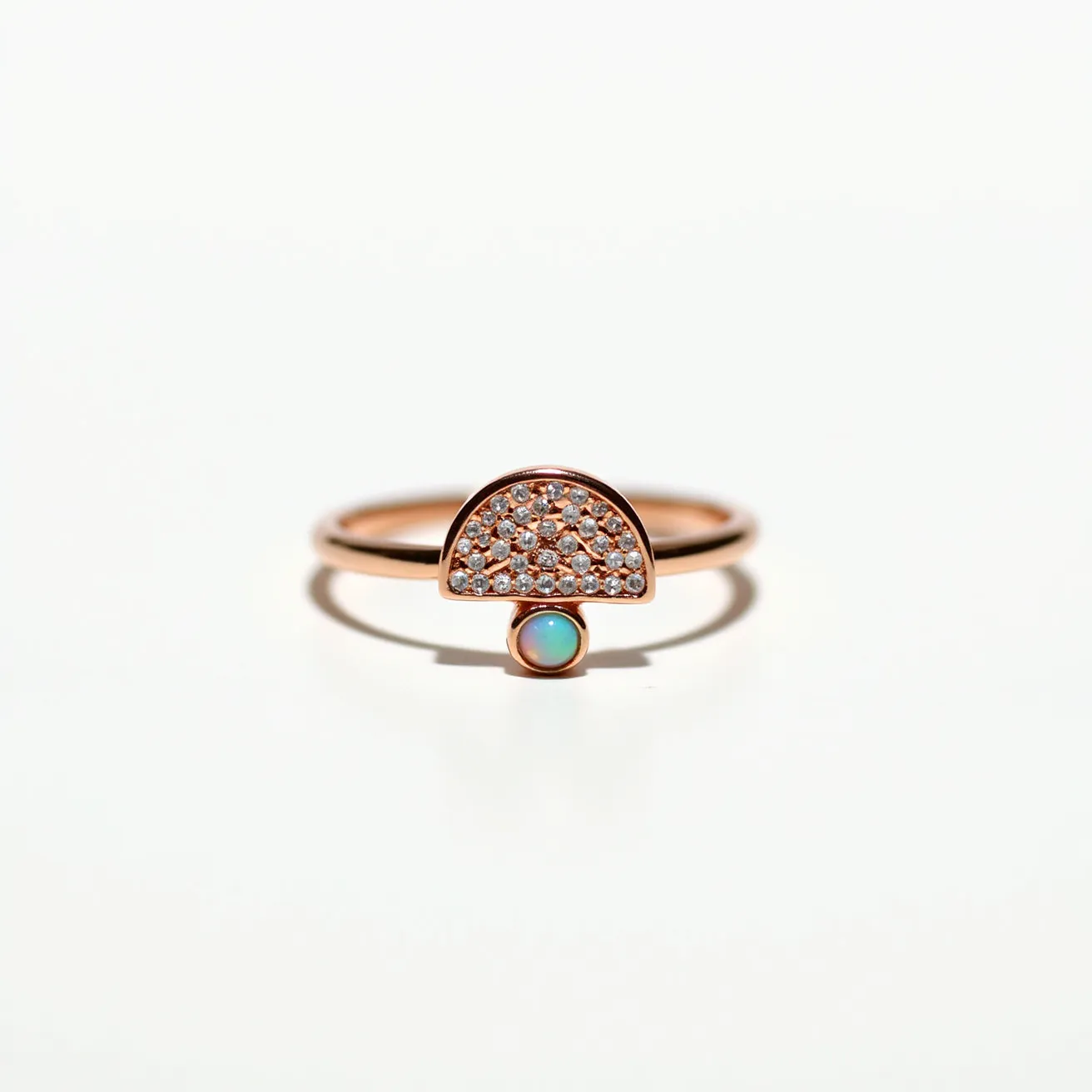 This mushroom ring features a sleek rose gold band with a distinctive mushroom-shaped motif as its centerpiece. The cap of the mushroom is adorned with numerous small, round-cut diamonds set in a pave style, creating a shimmering, textured surface. Beneath the cap, a single round opal is bezel-set, adding a burst of iridescent color that contrasts beautifully with the sparkle of the diamonds. The minimalist design highlights the elegance of the materials, with a smooth, continuous band that lacks any additional clasps or attachments.