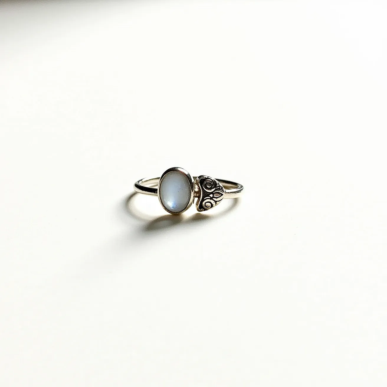 This mushroom ring features a delicate design crafted from silver, showcasing intricate detailing that resembles a mushroom cap. It is adorned with an oval-shaped gemstone, likely a moonstone, known for its subtle, iridescent sheen. The stone is set in a classic bezel setting, providing a secure hold and an elegant profile. The band is slender and complements the organic, whimsical design of the mushroom motif, creating a harmonious balance between the metal and the gemstone elements.