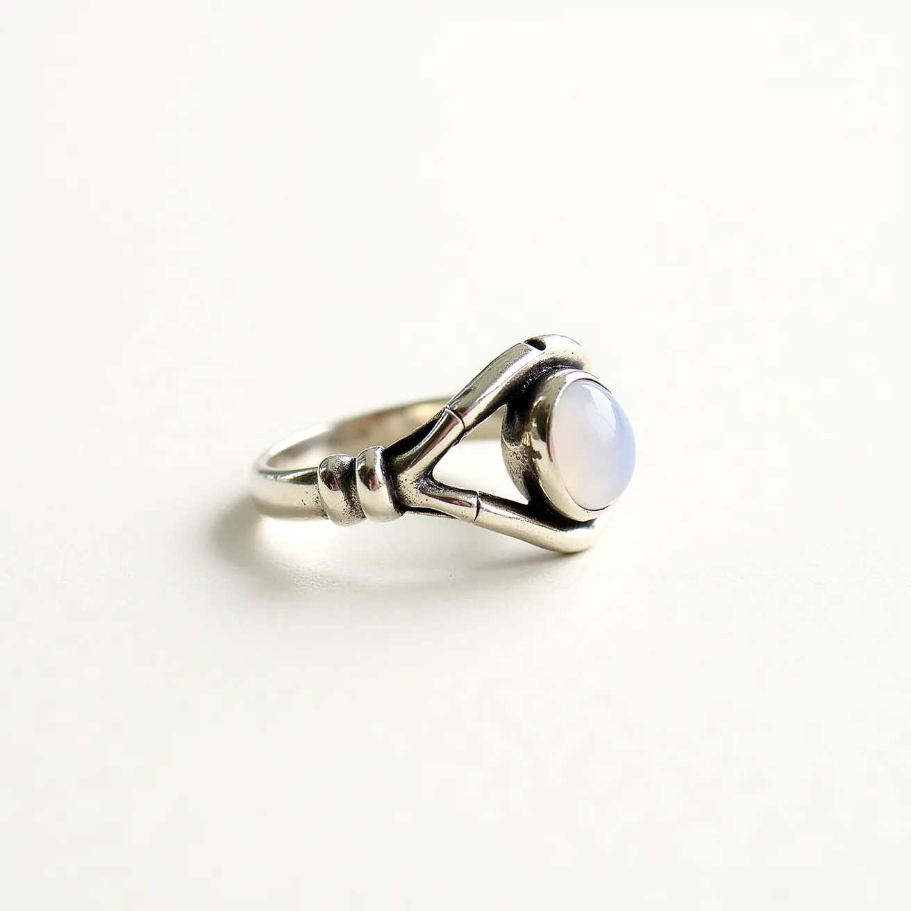 This mushroom ring showcases a sleek design in a polished silver metal, providing a sturdy and elegant band. At its center, a smooth, round cabochon gemstone, possibly moonstone or an opal, is securely set in a bezel setting, accentuating its iridescent and soft color. The setting is skillfully integrated into the band with a flowing design that subtly resembles delicate mushroom stems, adding a whimsical touch to the ring's appearance. The craftsmanship highlights a refined balance between modern simplicity and nature-inspired elements.