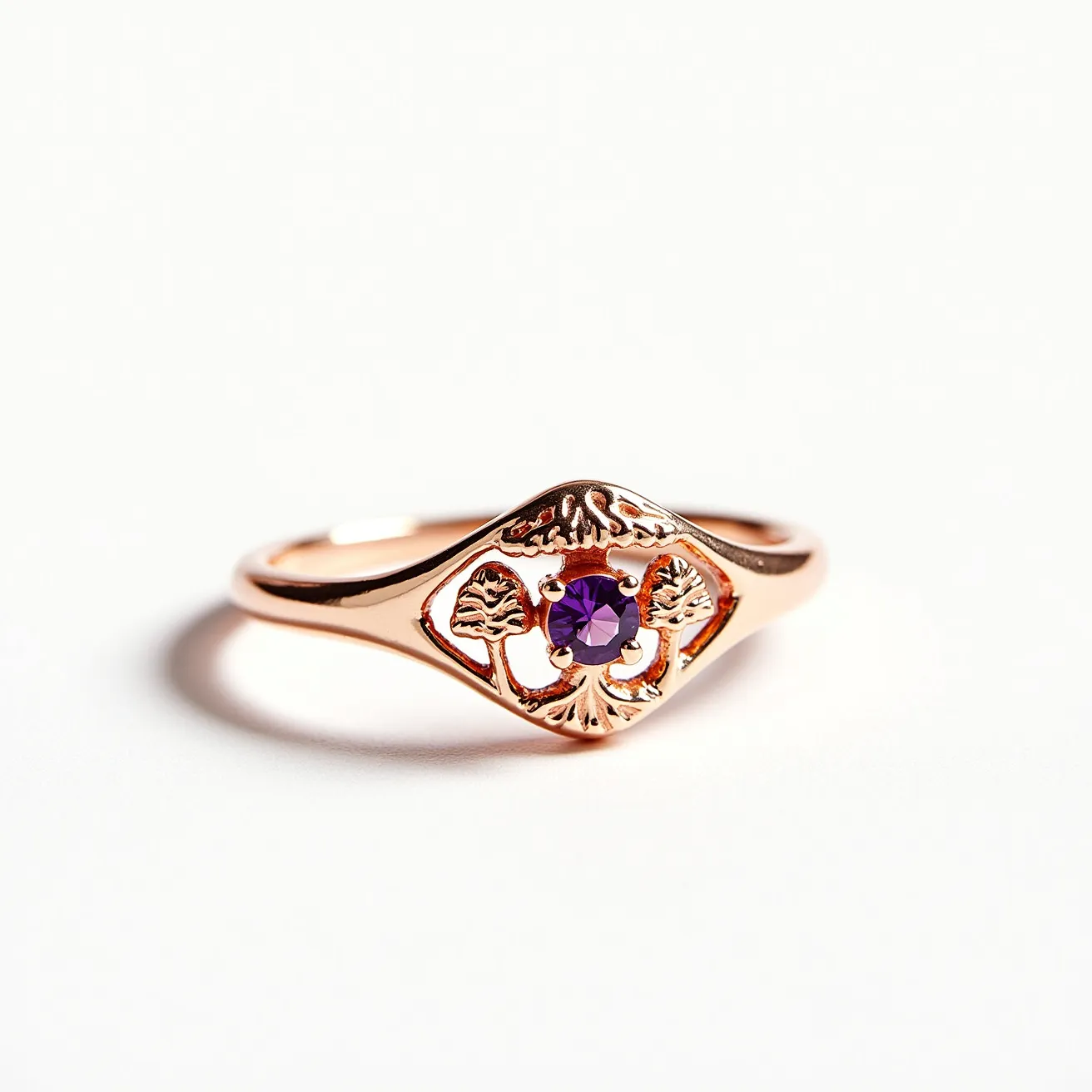 This mushroom ring is crafted from a material resembling rose gold, featuring an intricate design with small engraved mushrooms. At its center is a round-cut purple gemstone, securely held by a prong setting, which adds a vibrant focal point to the piece. The band is smooth and seamlessly transitions into the central motif, emphasizing the detailed artistry around the gemstone. The design is both elegant and whimsical, capturing attention with its unique blend of nature-inspired elements and refined craftsmanship.