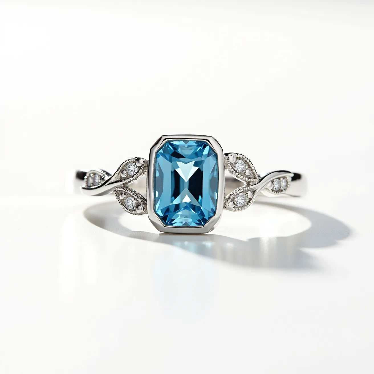 This November birthstone ring features a striking blue topaz gemstone, cut in a rectangular emerald style, set securely within a sleek bezel setting. The band is crafted from a polished silver-tone metal, enhancing the overall elegance of the piece. The design is accentuated with small round diamonds or diamond-like stones set in intricately detailed swirl motifs on either side of the central stone, adding a touch of sparkle. The ring's structure does not include a clasp, as it is a traditional circular band meant to slip onto the finger easily.