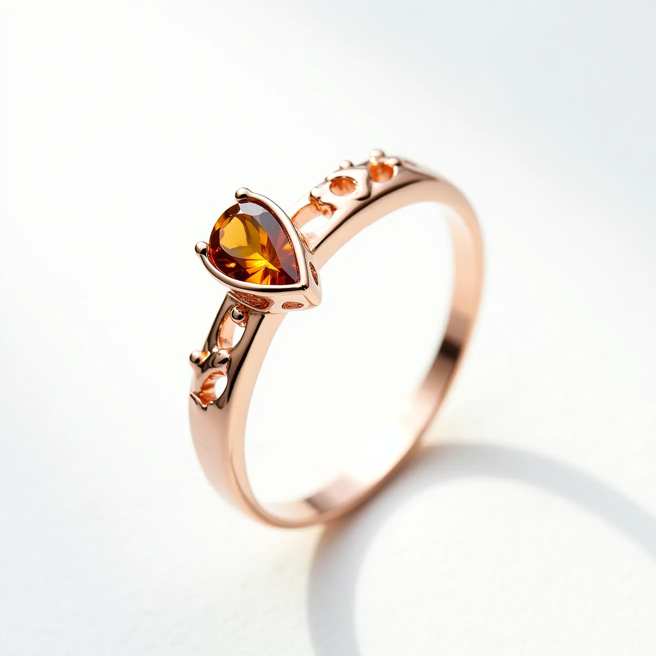 This November birthstone ring features a teardrop-cut citrine gemstone, known for its warm, amber hue, set elegantly in a polished rose gold band. The citrine is securely held by a bezel setting that accentuates its rich color and brilliance. The band is adorned with small, circular details along either side, adding an extra dimension of design without overshadowing the central stone. The smooth, continuous band of the ring ensures comfortable wear and elegance, making it an appealing piece for everyday wear or special occasions.