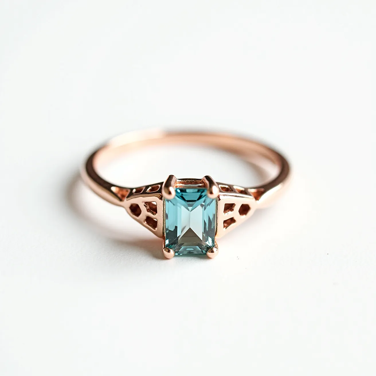 This November birthstone ring features a striking emerald-cut blue topaz, beautifully set in a four-prong setting that highlights its facets and deep color. The band is crafted from a warm rose gold, complementing the vibrant stone and adding an elegant touch. The design includes a delicate setting with decorative cutouts on either side of the gemstone, enhancing its sophisticated appearance. This ring showcases the importance of combining minimalism with intricate details, making it a perfect piece for those born in November who appreciate timeless beauty.