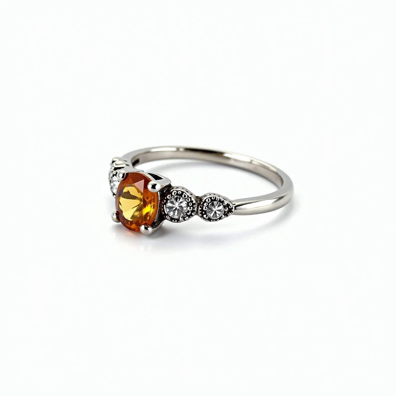 This November birthstone ring features a vibrant yellow-orange gemstone, likely a citrine, which is cut in an oval shape and secured by a four-prong setting. This centerpiece is flanked by two smaller round, clear stones, possibly diamonds or cubic zirconia, each set within their own unique mountings that add a decorative touch to the ring design. The band appears to be crafted from a shiny metal, possibly white gold or platinum, lending a sleek and elegant appearance to the overall piece. The seamless integration of the stones within the band highlights a careful attention to detail, making it not only a symbol of November's birthstone but also a stylish accessory.