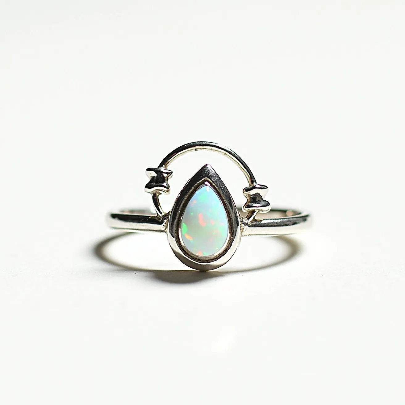 This October birthstone ring showcases a captivating opal, renowned for its play-of-color, set in a polished, teardrop shape. The opal is bezel-set, ensuring security and a sleek finish, while surrounded by a simple yet elegant silver band. The band features a unique celestial-inspired design with small star motifs on either side, adding a touch of whimsy and character to the piece. The overall design highlights the central opal, allowing its vibrant colors to take center stage.