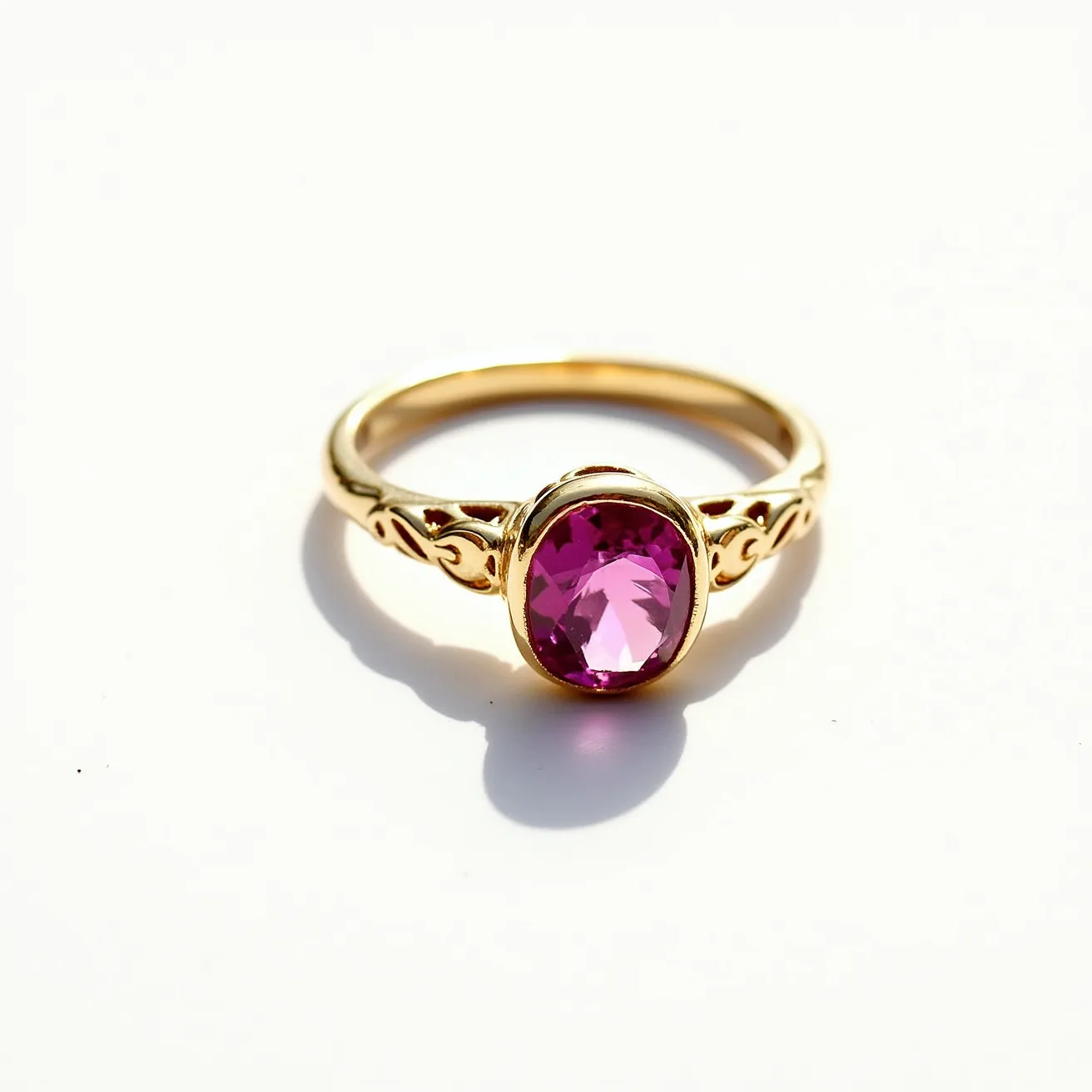 This October birthstone ring features a prominent oval-cut pink gemstone, likely a pink tourmaline, which is one of the birthstones for October. The gemstone is set in a bezel setting, securely encasing the stone within a smooth, metal band. The band itself appears to be crafted from gold, showcasing elegant, intricate designs on either side of the central stone. The combination of the richly colored gemstone and the ornate golden setting creates a piece that is both striking and classic in appearance.