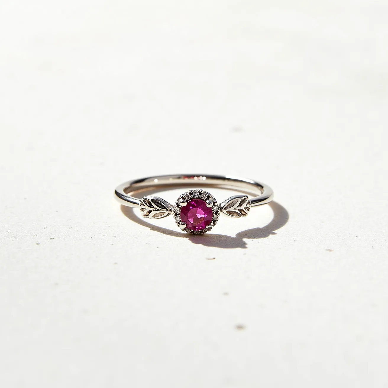 This October birthstone ring features a delicate design with a radiant pink tourmaline gemstone, which is the traditional birthstone for the month of October. The gem is cut in a round shape, set in a classic prong setting, and surrounded by a halo of tiny, sparkling accent stones that enhance the ring's elegance. The band is crafted from a sleek, polished metal that appears to be white gold or platinum, lending a modern and sophisticated finish to the piece. Flanking the central gem are two small leaf motifs, adding a touch of nature-inspired charm to the design. The absence of a clasp suggests a traditional ring band form, offering a seamless and continuous look.