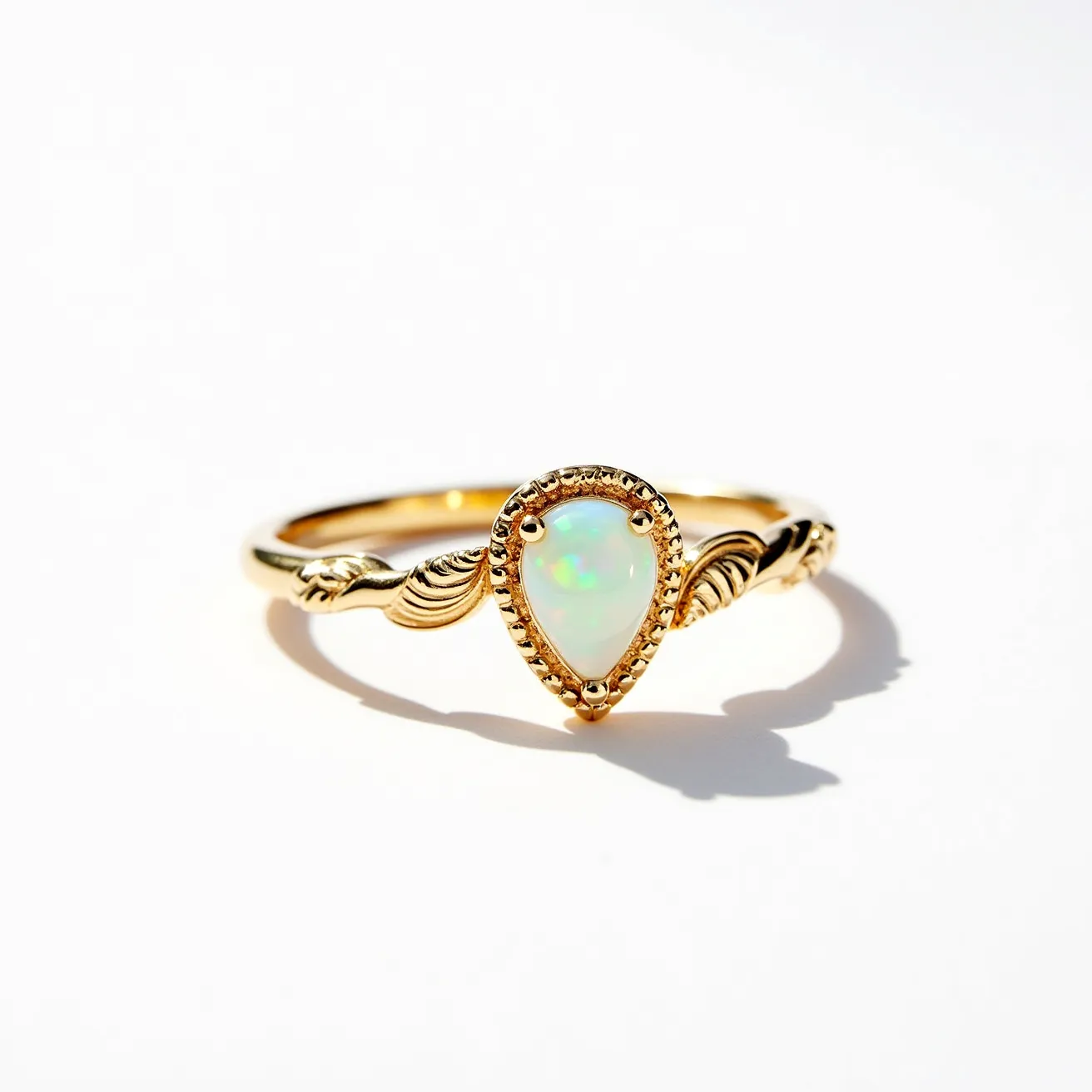 This October birthstone ring features a pear-shaped opal as the centerpiece, showcasing its characteristic play-of-color. The opal is set in a bezel setting, securely held by a gold band adorned with intricate twisted detailing along the shank. The ring showcases a delicate and refined design, enhancing the natural beauty of the opal, which is the birthstone for October. The gold material of the band complements the iridescent hues of the opal, creating a harmonious and elegant aesthetic.