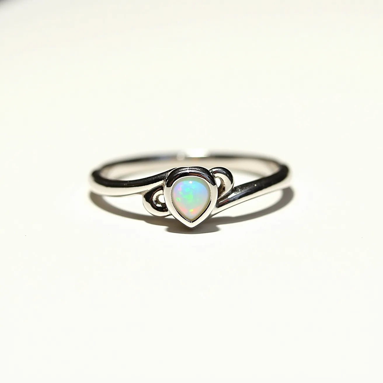 This opal engagement ring features a central opal gemstone cut in a teardrop shape, set within a minimalist bezel setting. The opal displays a play of colors, characteristic of high-quality opals. The band is crafted from a polished silver or white gold metal, adding a sleek and modern appearance to the design. The simple, elegant setting allows the opal to be the focal point of the ring, enhancing its beauty and iridescence.