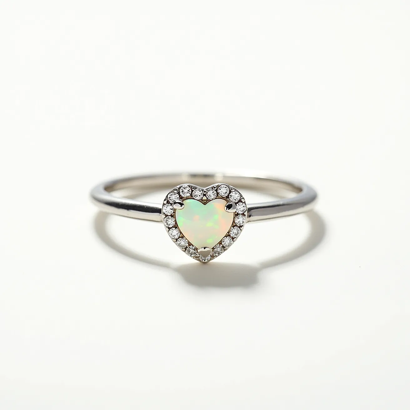 This opal engagement ring features a central heart-shaped opal as its main gemstone, exhibiting a vibrant play of color typical of high-quality opals. The opal is elegantly surrounded by a halo of small round-cut diamonds, enhancing its brilliance and adding a layer of sophistication. These diamonds are set in a prong setting that secures the stones while allowing maximum light exposure. The band of the ring appears to be crafted from a polished metal, possibly white gold or platinum, complementing the opal and diamonds with its sleek and reflective surface. The combination of the opal and diamond accents creates a piece that is both unique and visually captivating.