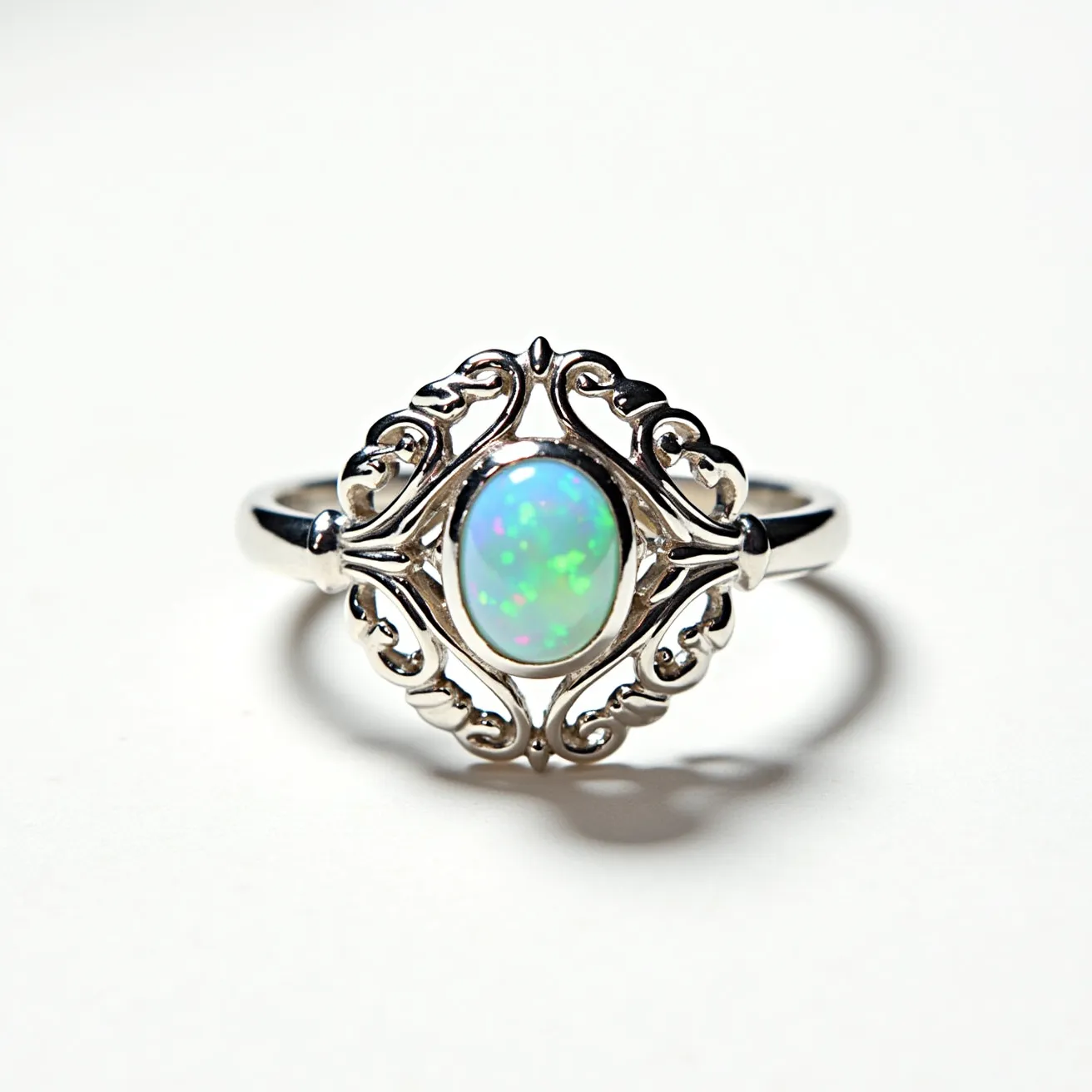 This opal ring features a captivating oval opal at its center, displaying a play of colors typical of this gemstone, with flashes of green and blue. The opal is set within an intricate silver setting that holds it securely, showcasing detailed filigree work that adds an elegant touch. The band is crafted from polished silver, providing a sleek and complementary backdrop to the fiery opal centerpiece. The design lacks any additional stones, allowing the opal's vibrant hues to remain the focal point of the piece. The ring's overall design is ornate yet balanced, combining the natural beauty of the opal with the craftsmanship of the metalwork.