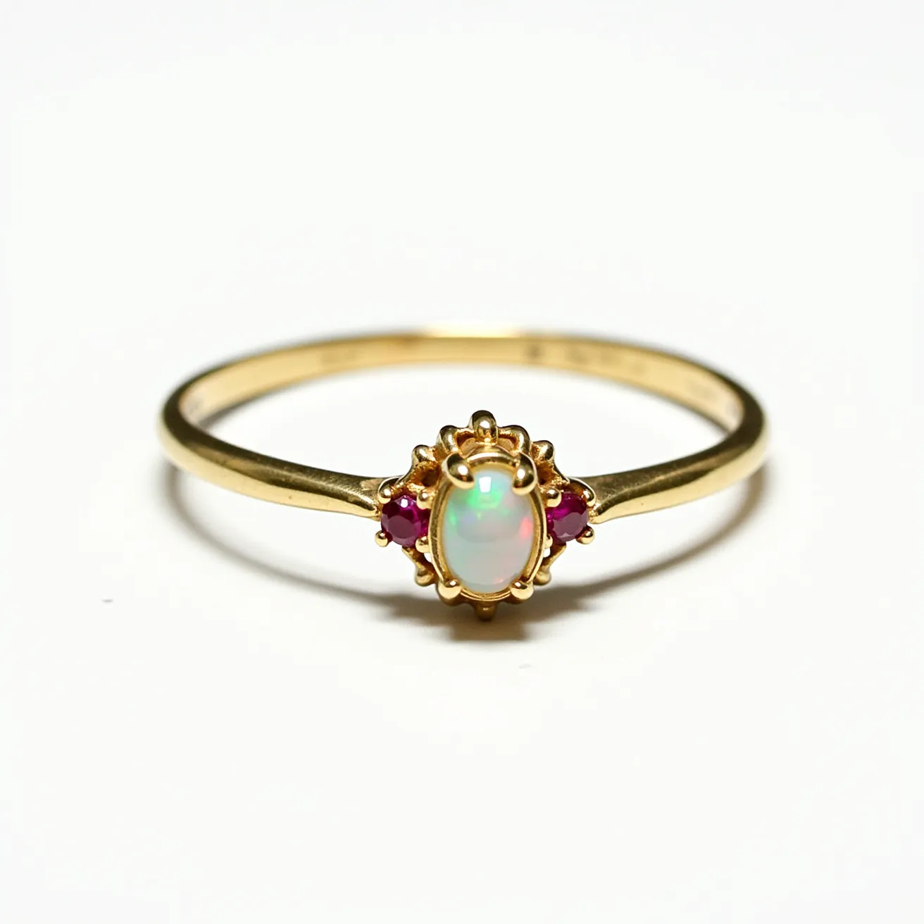 This opal ring features a delicate gold band that supports an oval opal as the centerpiece. The opal displays a play of colors characteristic of the gem, and it is held securely in place by a decorative claw setting. Flanking the opal are two small ruby stones, adding vibrant contrast and intricately set within the gold band. The ring's elegant design showcases the center opal while the rubies enhance its overall aesthetic appeal.