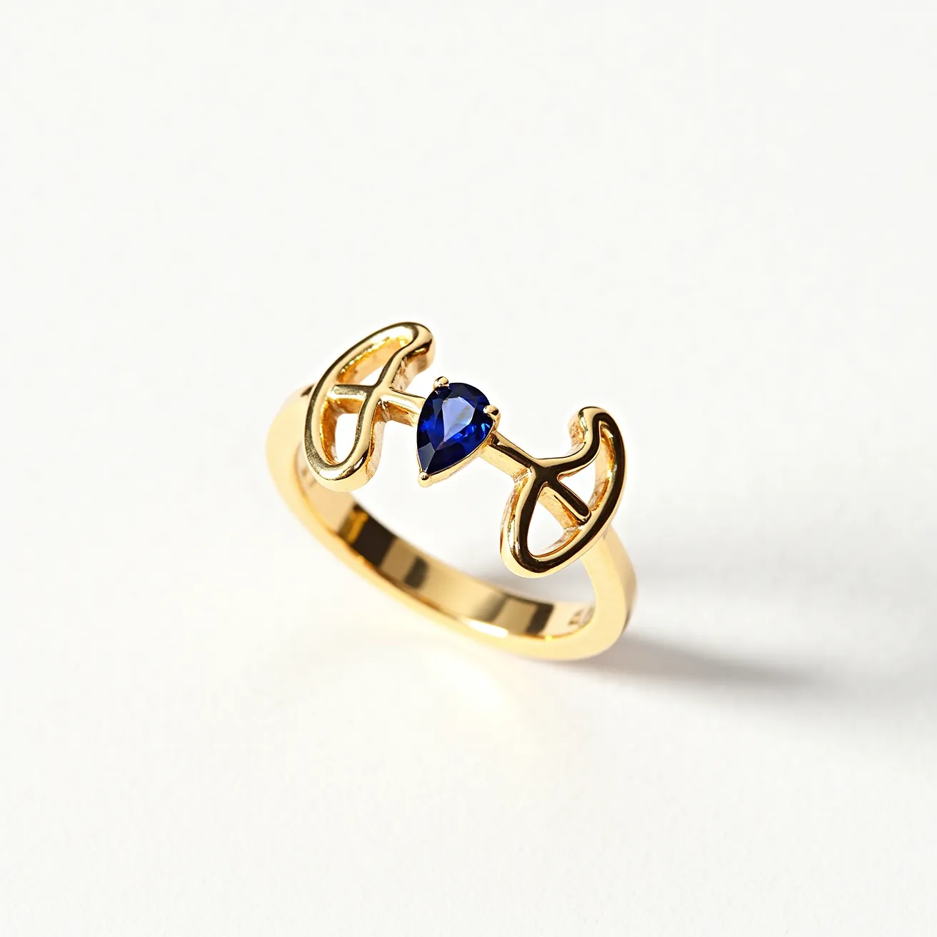 This open ring is crafted from a gold material, featuring a distinctive design that frames a central, pear-cut sapphire gemstone. The sapphire is securely set between the open ends of the ring, which resemble stylized, flowing shapes, adding an elegant and unique element to the piece. The sleek, polished texture of the gold enhances the deep blue of the sapphire, making it the focal point of the ring. The overall composition of the ring showcases a blend of modern aesthetics with a touch of classic elegance.