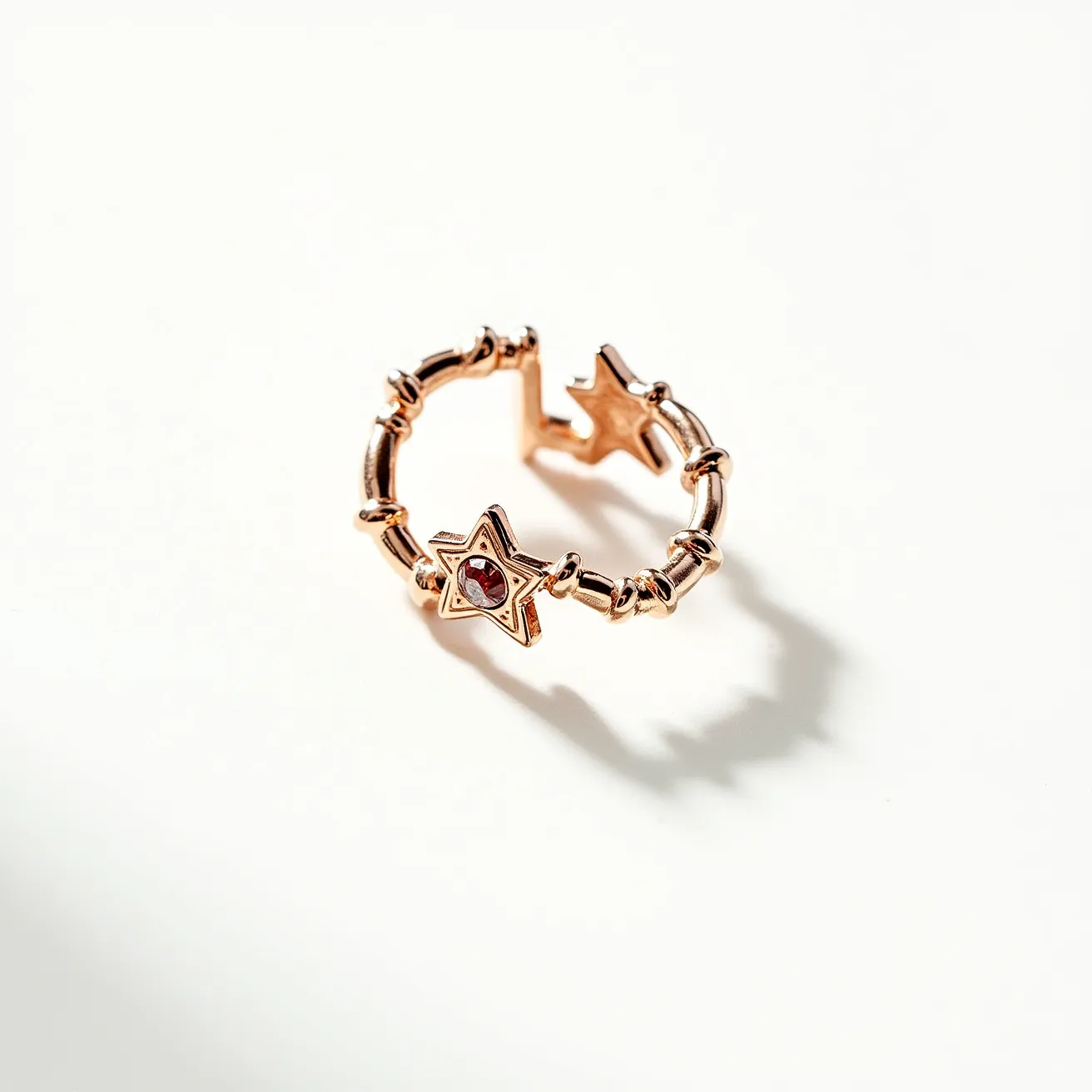 This open ring is crafted from a rose gold-toned metal, featuring a series of delicate, evenly spaced beads along its band. At its center is a prominent star-shaped design that holds a small, round-cut red gemstone set in a bezel setting. The open design of the ring is accented by another star at one end, mirroring the central motif and enhancing the overall celestial theme. The combination of the rose gold material and the deep red gem creates an elegant contrast, perfect for a bold yet refined aesthetic.