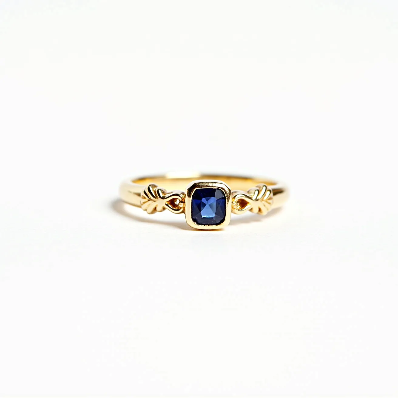 This open ring features a gold band with an intricate design incorporating decorative details. At the center, a deep blue, square-cut gemstone is held securely within a bezel setting, adding an elegant contrast to the warm gold tones. The ring does not have a traditional clasp or attachment, given its open-ended design. The combination of the gold and the blue gemstone creates a classic and timeless appearance.