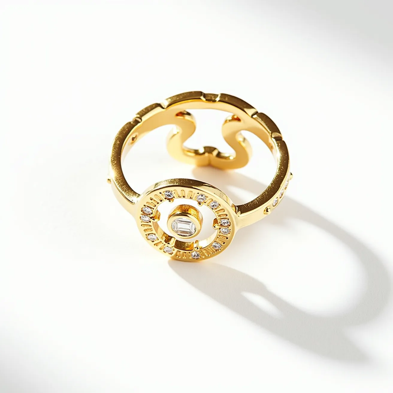 This open ring showcases a gold-toned metal band featuring an intricate design with a circular motif at its center. The motif is set with a baguette-cut stone, likely a diamond or a similar stone, surrounded by smaller round-cut stones evenly arranged around the perimeter, creating a halo effect. The smooth finish of the metal adds to the elegance, while the open design gives it a modern and adjustable feel. The stones are securely set, possibly in a bezel or pave setting, ensuring stability and style without any visible clasps or attachments.