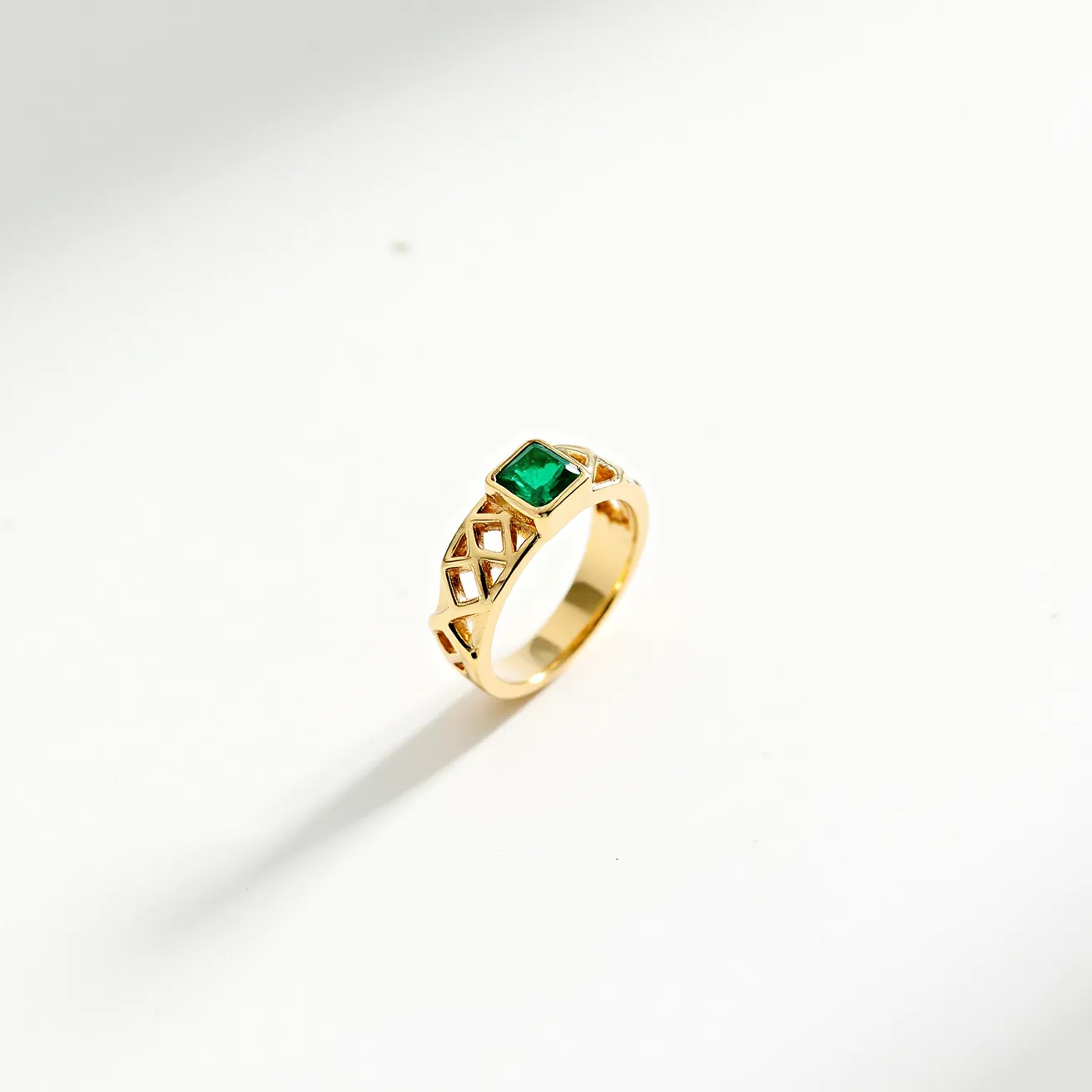 This open ring features a square-cut green gemstone centrally set, likely an emerald, held securely in a bezel setting. The band is crafted from gold and showcases a lattice-like design with open geometric patterns, adding an elegant and contemporary touch. The ring design does not include any additional clasp or attachment, indicating a sleek, minimalist aesthetic. The choice of materials and craftsmanship indicate a high-quality piece suitable for both daily wear and special occasions.