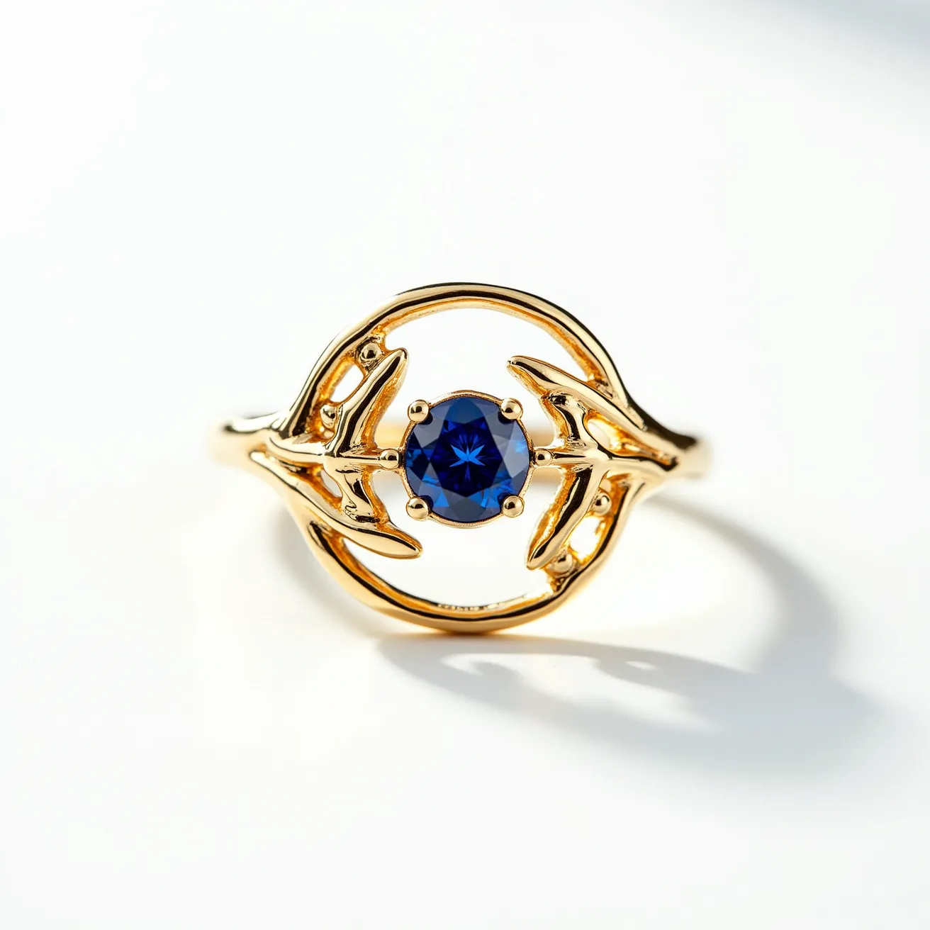 This open ring features a delicate design crafted from gold, characterized by an intricate, leafy pattern that encircles a central gemstone. The gemstone is a deep blue sapphire, expertly cut in a round shape, and is securely held in place by a prong setting. There are no additional clasps or attachments, allowing the detailed goldwork and vibrant sapphire to be the focal points of this elegant jewelry piece.