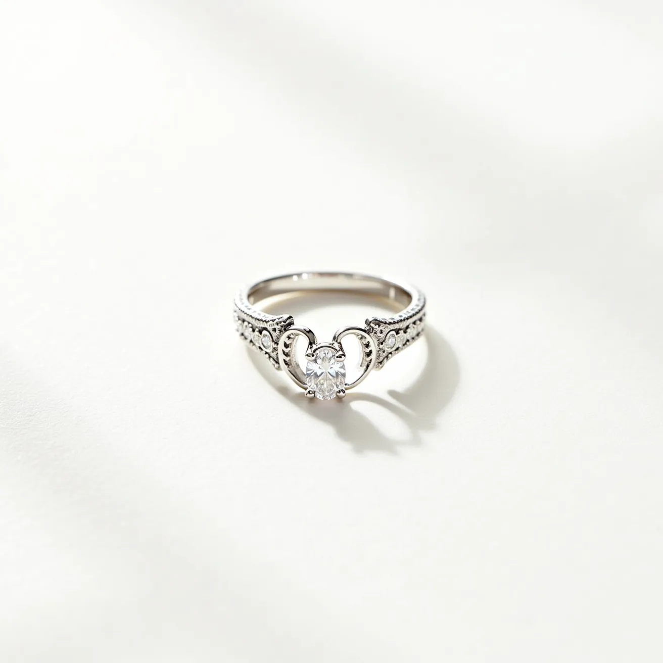 This open ring features a polished silver band adorned with intricate detailing along the shoulders, giving it a vintage-inspired look. At its center, a round-cut diamond is prominently set in a prong setting, enhancing its brilliance and allowing maximum light reflection. The band includes smaller stones embedded into the metal, adding to the ring's overall elegance and sparkle. The design allows the central diamond to sit elevated, framed by elegant silver curves, contributing to the ring's sophisticated aesthetic.