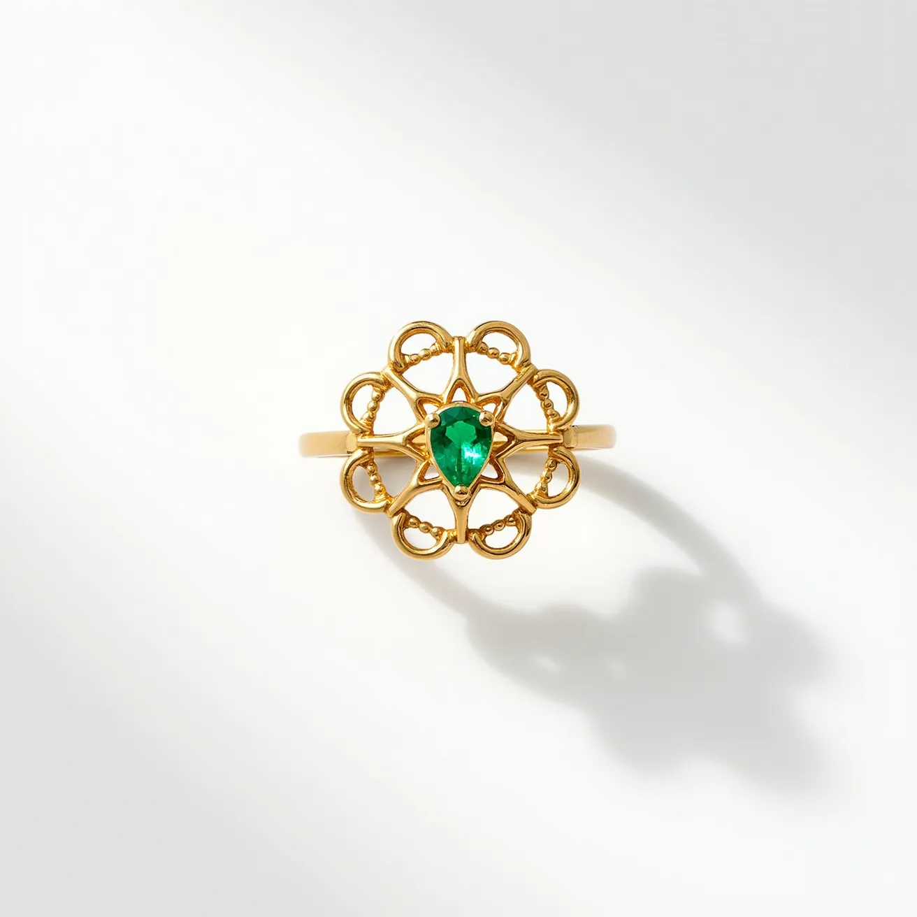 This open ring features a prominent design crafted from what appears to be gold, forming an intricate floral pattern. At the center, a pear-cut green gemstone, likely an emerald, is securely set, enhancing its elegant and vivid appearance. The gold metalwork exhibits delicate loops and curves that add a decorative element to the piece. The gemstone is set in a prong setting, allowing for maximum visibility and light reflection. The absence of a traditional clasp or closure keeps the design open and continuous, emphasizing the central motif and gemstone.