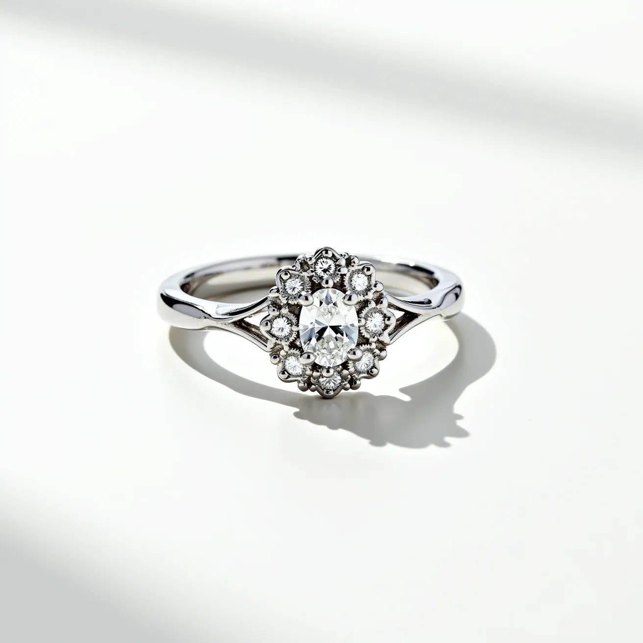 This oval diamond ring features a central oval-cut diamond encircled by a halo of smaller round diamonds arranged in a cluster setting, creating a flower-like appearance. The band is crafted from a polished metal, likely white gold or platinum, which complements the brilliance of the diamonds. The central stone is securely set, held in place by prongs that allow for maximum light reflection, while the surrounding stones add additional sparkle and enhance the ring's overall elegance. The band is smooth and narrows slightly towards the setting, drawing attention to the intricate design of the gemstone arrangement.