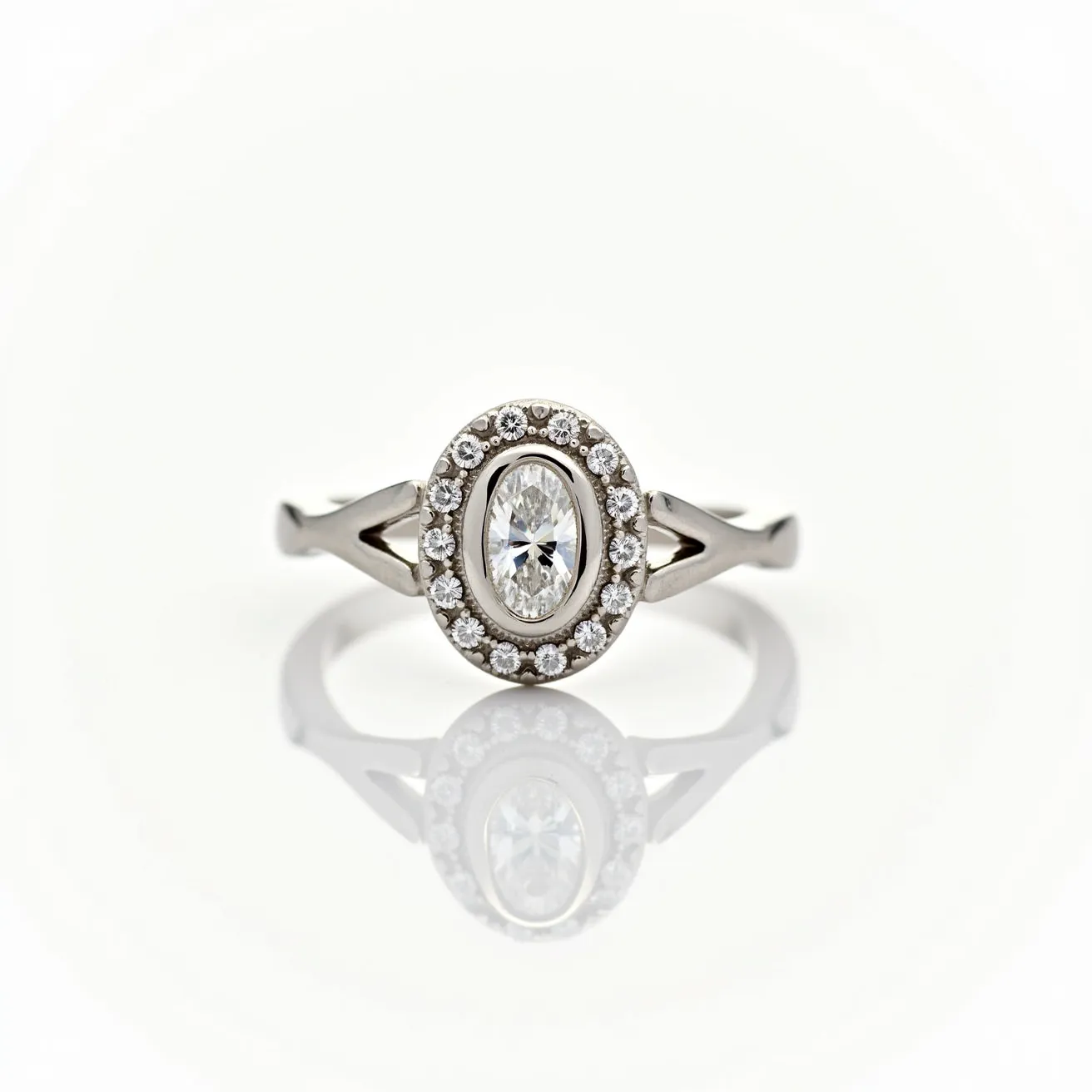 This oval diamond ring features a central oval-cut diamond elegantly surrounded by a halo of smaller round diamonds, enhancing its brilliance and visual appeal. The setting is crafted from a polished metal, likely white gold or platinum, which complements the clarity and sparkle of the diamonds. The ring's band splits to embrace the halo setting with an intricately designed shank that adds a touch of sophistication and modern flair. Overall, the combination of the central stone and the surrounding accent diamonds creates a classic yet contemporary piece of jewelry that exudes elegance.