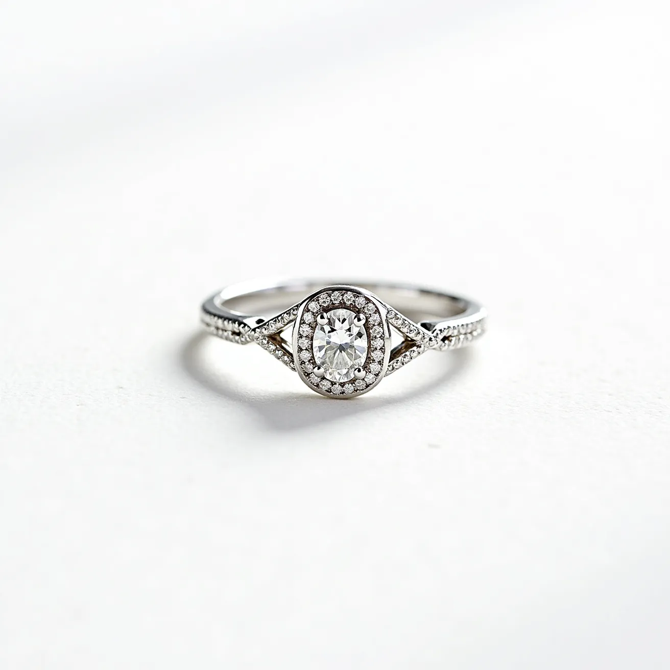 This oval diamond ring features a central oval-cut diamond encircled by a halo of smaller round diamonds, enhancing its brilliance and elegance. The setting appears to be made of polished white gold or platinum, which complements the sparkle of the diamonds. The band showcases additional smaller diamonds, emphasizing a sophisticated design that adds to the overall luxury of the piece. The ring's craftsmanship highlights meticulous attention to detail, with the halo and band settings intricately holding each gem securely, creating a striking and timeless accessory.