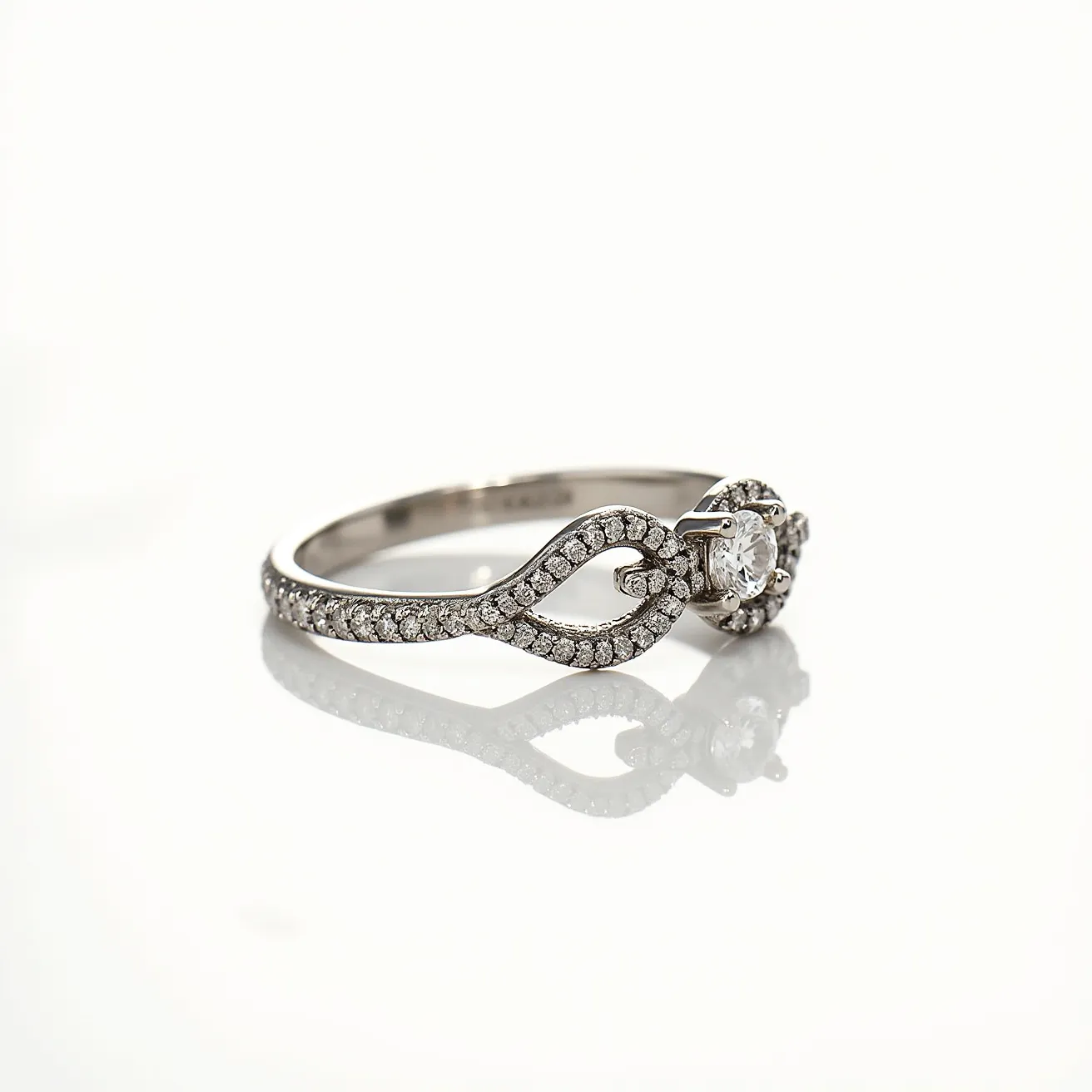 This pave diamond ring features a white metal band, likely platinum or white gold, adorned with numerous small, closely set round diamonds that create a continuous sparkle throughout. The centerpiece of the ring is a larger round brilliant-cut diamond, which is secured in a prong setting, highlighting its brilliance. The intertwining design of the band adds an elegant and sophisticated touch, enhancing the overall aesthetic appeal of the piece. This ring exemplifies fine craftsmanship and a classic yet modern design, making it an exquisite choice for special occasions.