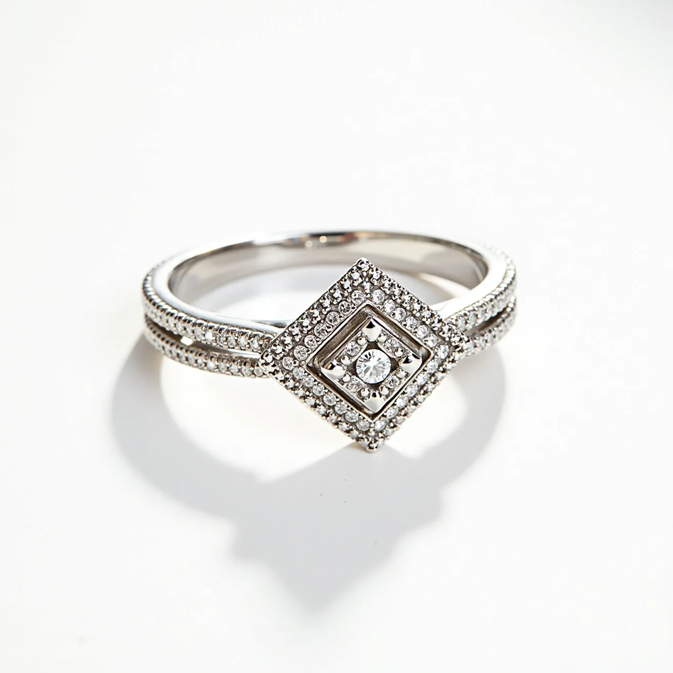 This pave diamond ring showcases a central round-cut diamond set within a square design, elegantly bordered by smaller pave-set diamonds. The ring is crafted from a lustrous white metal, likely platinum or white gold, which enhances the brilliant sparkle of the diamonds. The band features intricate detailing with dual rows of pave-set diamonds, adding to the ring's opulent aesthetic. The setting is secure, with the central stone held in place by a four-prong setting, designed to highlight the diamond's brilliance while ensuring durability. The overall design exhibits a harmonious blend of luxurious materials and meticulous craftsmanship.