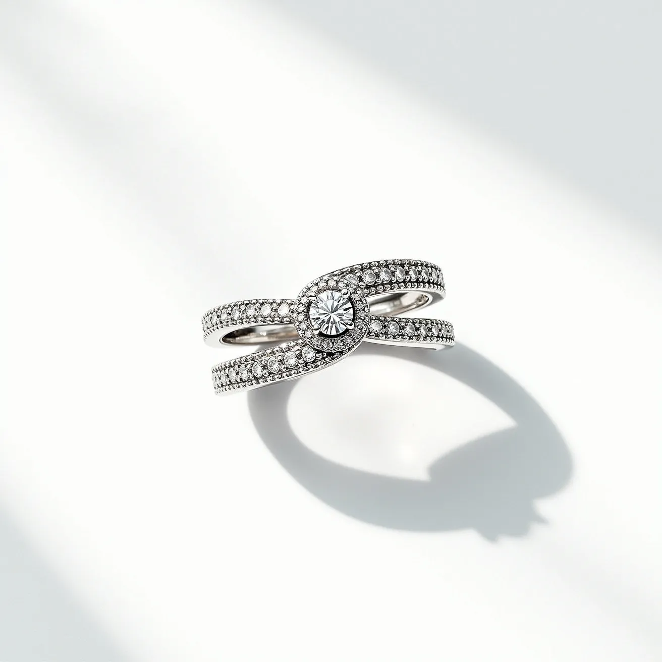 This pave diamond ring showcases a sophisticated design featuring a central round brilliant-cut diamond set in a bezel setting. Surrounding the central stone and adorning the bands are numerous smaller pave-set diamonds, enhancing the ring's sparkle and elegance. The ring is crafted from lustrous white metal, likely white gold or platinum, offering a refined backdrop that complements the shimmering diamonds beautifully. Its intertwined band design adds a unique and intricate aesthetic, creating a sense of fluidity and continuity.