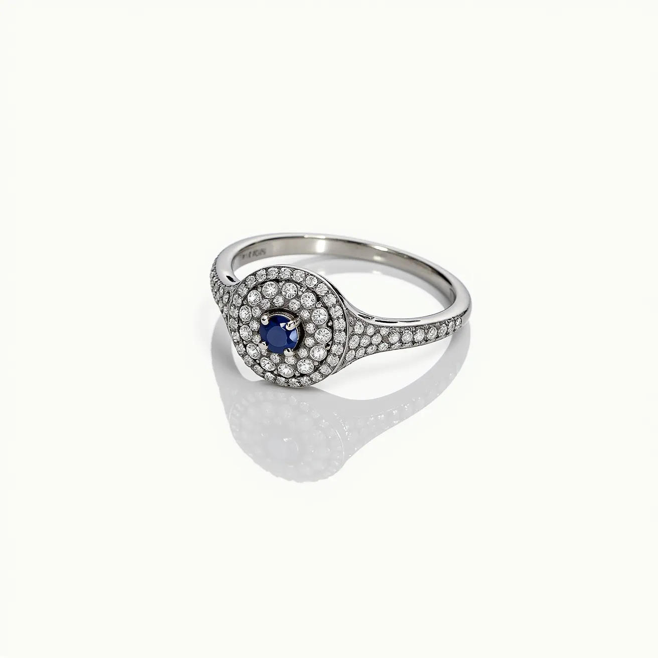 This pave diamond ring features a central round sapphire, set prominently with prongs at the heart of the design. The sapphire is surrounded by a halo of small, meticulously set pave diamonds that extend partially down the shoulders of the ring, enhancing its brilliance and elegance. The band appears to be made of white gold or platinum, providing a sophisticated and sturdy setting for the gemstones. The combination of the deep blue sapphire and sparkling diamonds creates a timeless and luxurious piece.