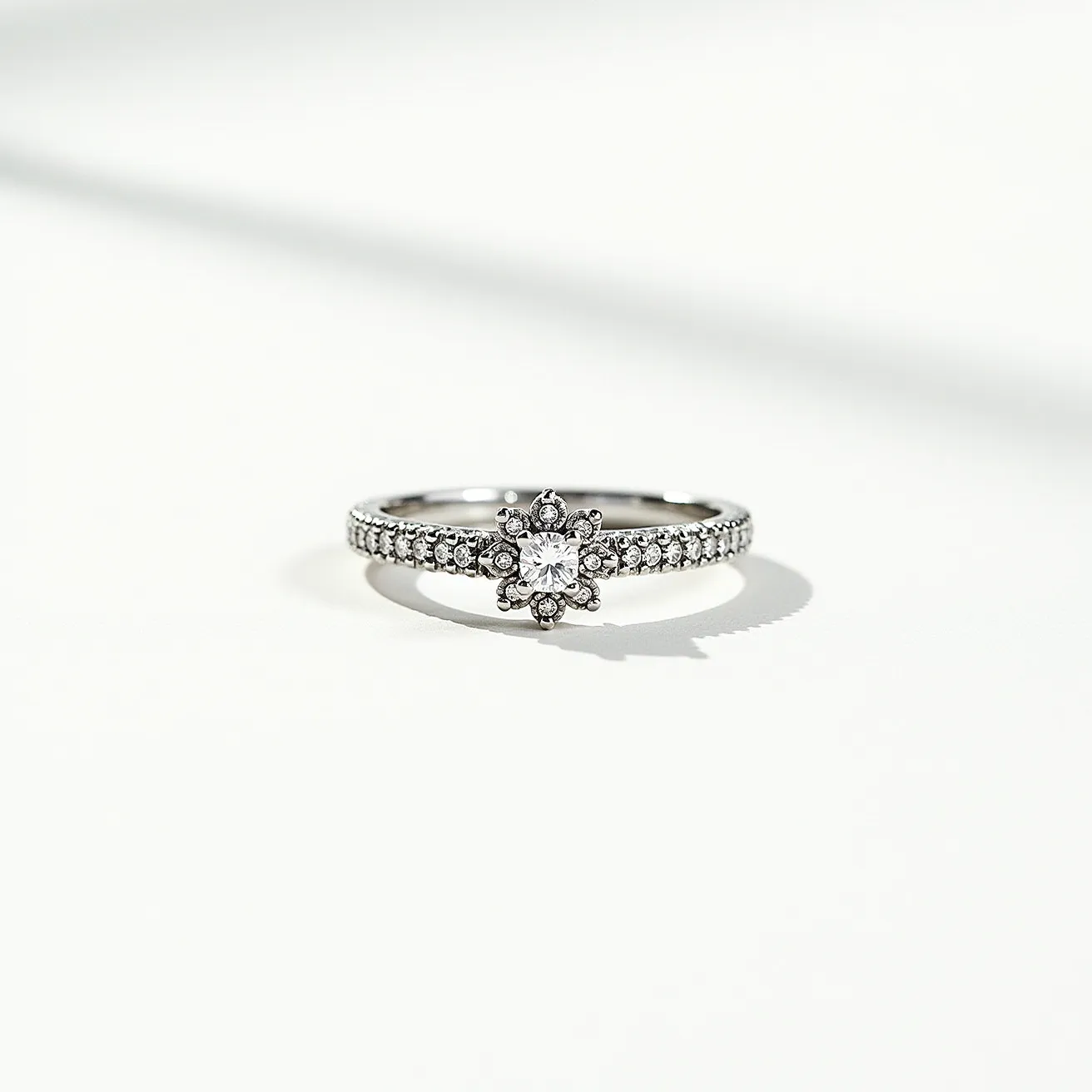 This pave ring features an elegant design with a central square-cut gemstone, likely a diamond, set prominently in a prong setting. Surrounding the main stone is a halo of smaller round stones, enhancing its sparkle and creating a floral appearance. The band is encrusted with similarly cut round stones in a pave setting, adding a continuous shimmer along its circumference. The band and setting are crafted from a white metal, possibly white gold or platinum, providing a sleek, sophisticated look. The combination of materials and design elements gives the ring a classic yet contemporary elegance.