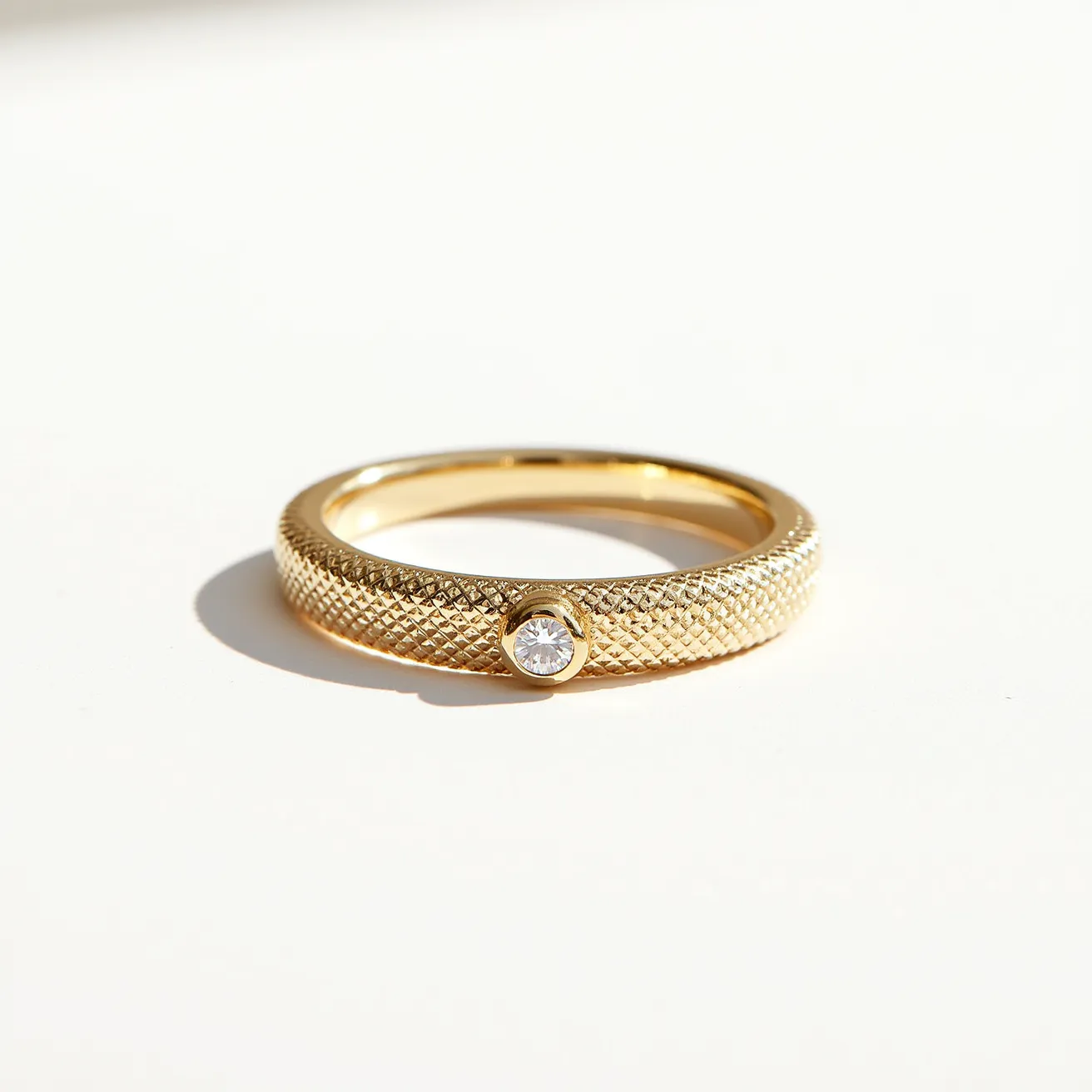 This pave ring features a textured gold band with a single round-cut diamond set in a bezel setting. The gold band displays a detailed pattern that enhances its visual appeal, while the diamond provides a focal point with its brilliance. The ring is crafted without any visible clasps or attachments, showcasing a seamless design. The combination of the gold and diamond exudes elegance and sophistication, making this piece a stylish accessory.