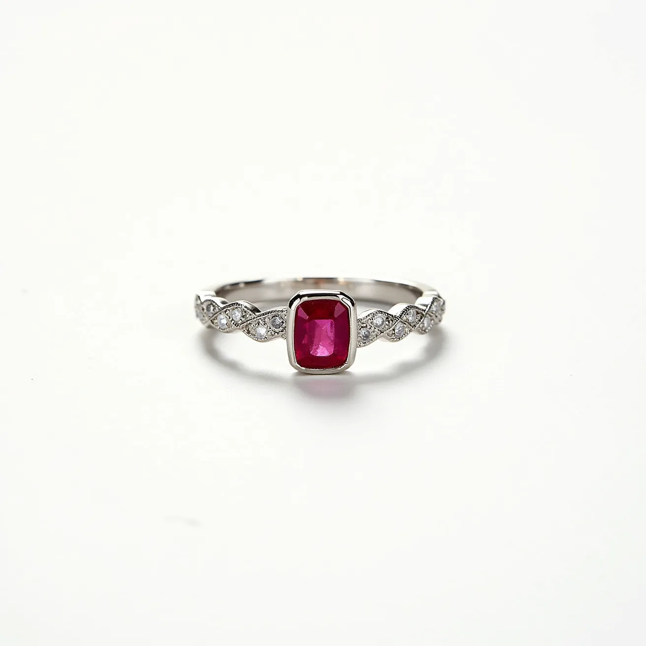 This pave ring features a central cushion-cut ruby, showcasing a vibrant red hue, set in a bezel setting. The band appears to be crafted from a polished white metal, likely platinum or white gold, and is adorned with small round diamonds arranged in a twisted pave configuration. This intricate design enhances the overall elegance and sparkle of the ring. The combination of the rich ruby and sparkling diamonds creates a striking and luxurious appearance.