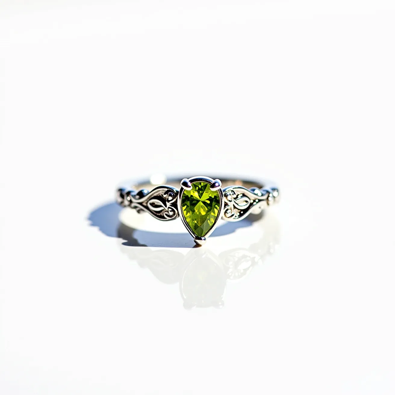 This peridot engagement ring features a vibrant pear-cut peridot as its centerpiece, set in an ornate, intricate silver band that showcases delicate scrollwork on either side of the gemstone. The peridot is held securely by a prong setting, allowing light to enhance the stone’s natural green luster. The craftsmanship of the silver band accentuates the gemstone’s beauty, creating a harmonious balance between classic elegance and a touch of unique artistry. The overall design of the ring suggests a blend of traditional and contemporary styles, making it a striking choice for an engagement ring.