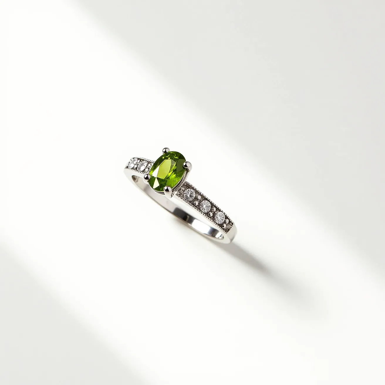 This peridot engagement ring features a striking oval-cut peridot as the central gemstone, with its vibrant green hue elegantly showcased. The stone is securely held by a prong setting, allowing maximum light to reflect through the peridot. The band is crafted from a lustrous metal, possibly gold or platinum, and is adorned with a series of small round-cut diamonds embedded along its side. These diamonds add a touch of brilliance and contrast beautifully with the central gemstone, enhancing the ring's overall elegance and sophistication.