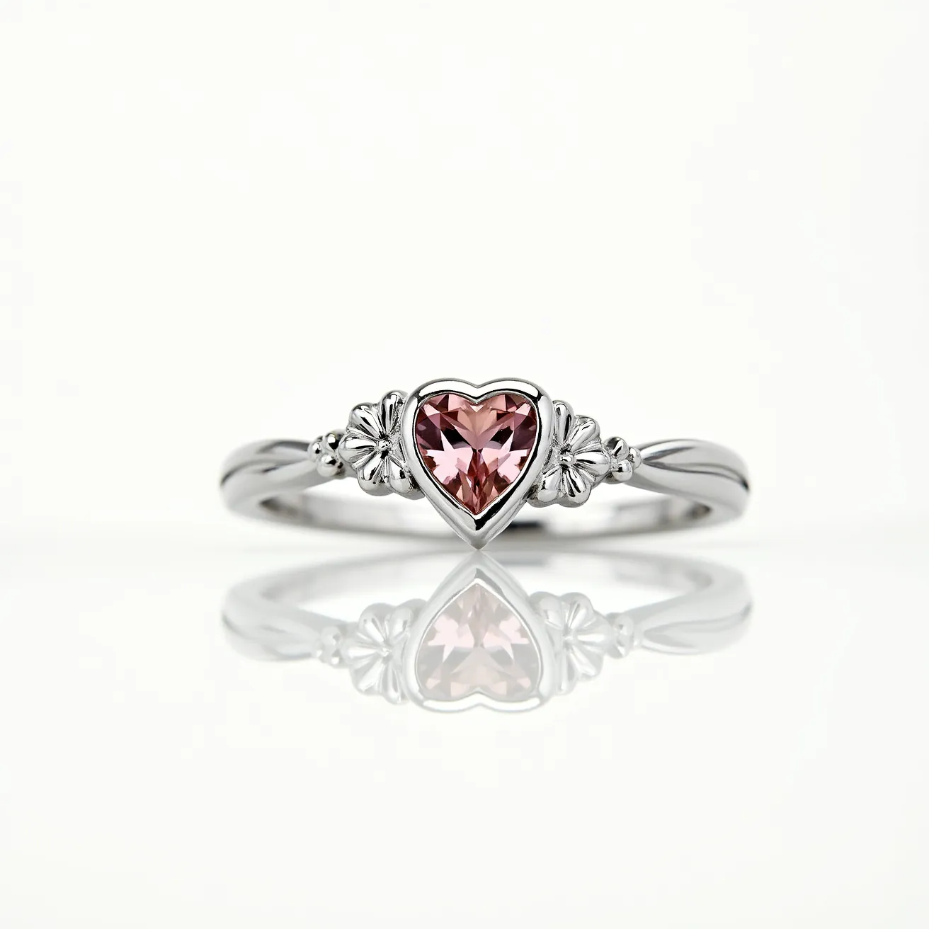 This pink heart ring features a central heart-shaped pink gemstone, likely a sapphire or tourmaline, finely cut to enhance its sparkle and elegance. The stone is securely set in a bezel setting, which provides a smooth and protective edge. The band appears to be crafted from a polished silver or white gold metal, characterized by a delicate design that includes small, ornate floral motifs flanking the gemstone on either side. The overall design combines an elegant aesthetic with functional craftsmanship, ensuring both beauty and durability.