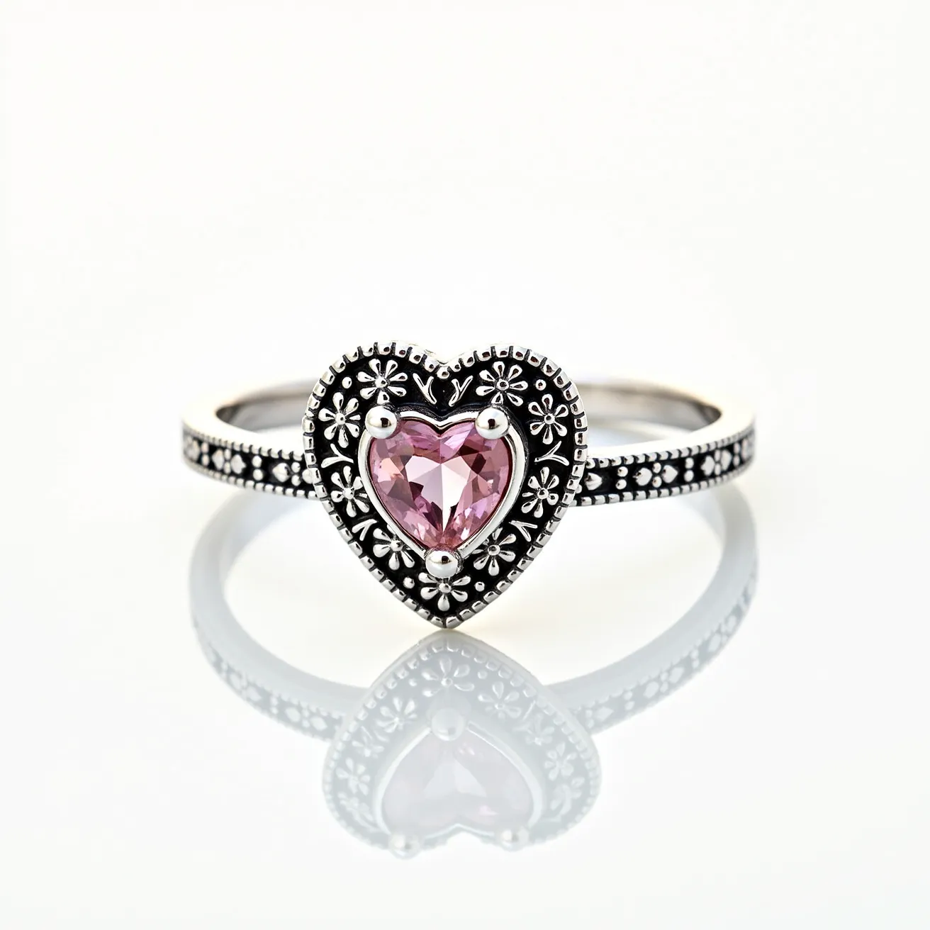 This pink heart ring features a captivating pink heart-shaped gem set at its center, secured by a four-prong setting. The stone exhibits a brilliant cut, enhancing its sparkle and allure. Surrounding the gem is a decorative heart-shaped metal frame adorned with intricate floral and beaded patterns, adding a touch of elegance and charm to the design. The band itself is detailed with a series of small, evenly spaced beads, contributing to its overall ornate appearance. The craftsmanship and detail suggest a delicate and romantic style, making it a unique and beautiful piece of jewelry.