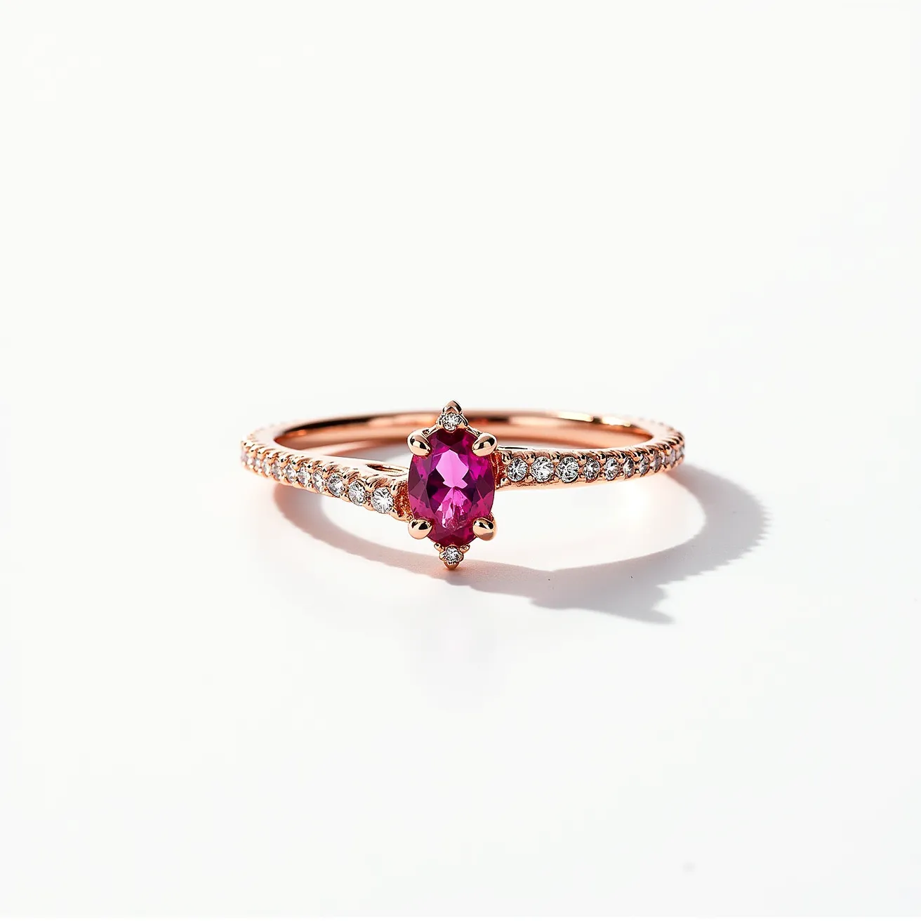 This pink sapphire ring features a central oval-cut pink sapphire set in a delicate prong setting. The band appears to be made of rose gold, enhancing the warmth of the pink sapphire. Flanking the main stone, a row of small round-cut diamonds is set into the band, adding sparkle and elegance. The diamonds are likely set using a pavé or bead setting, ensuring the ring retains a sleek and refined appearance.