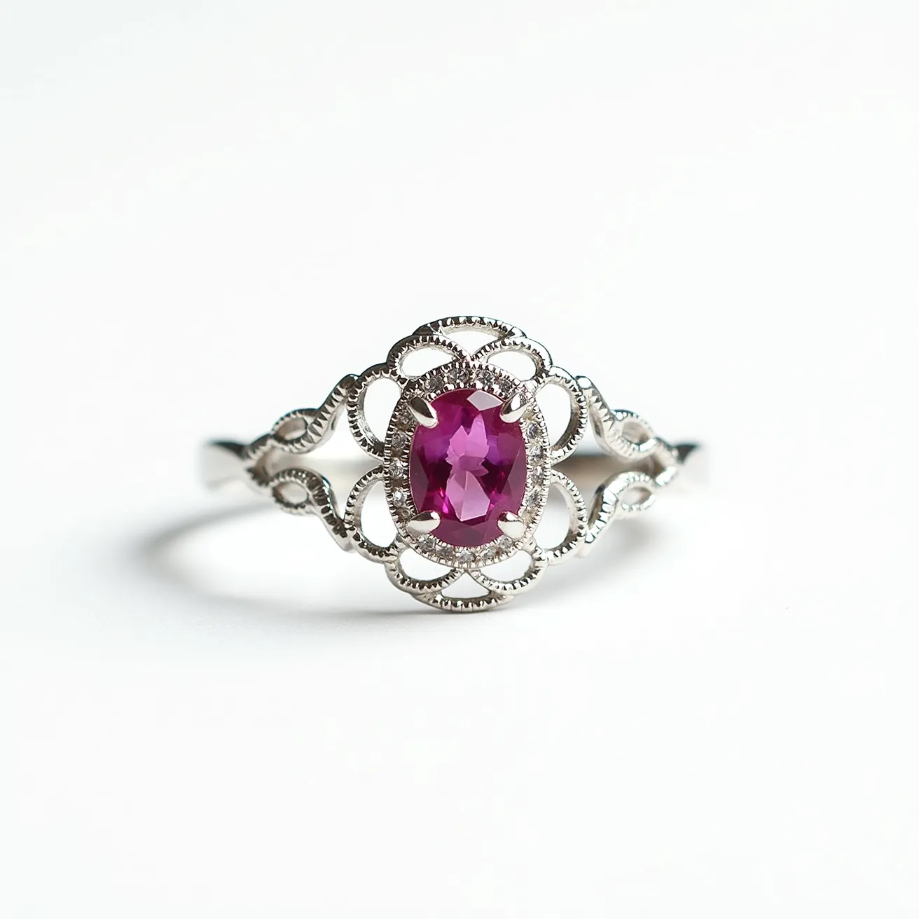 This pink sapphire ring features an oval-cut pink sapphire as the centerpiece, elegantly set within a delicate and intricate silver filigree design. The gemstone is secured by four prongs, showcasing its vibrant hue and clarity. The filigree setting adds a vintage charm, enhancing the overall elegance and sophistication of the piece. The ring band, likely made of a polished metal such as white gold or platinum, complements the vivid sapphire while providing a sturdy and stylish structure. The design reflects a blend of classic and contemporary aesthetics, perfect for adding a touch of luxury and color to any occasion.