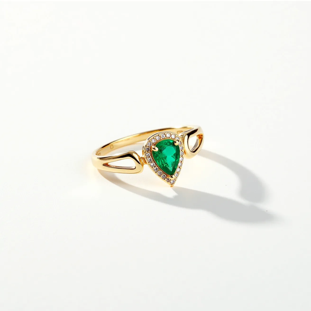 This pinky ring features a striking green pear-shaped gemstone, likely an emerald, set in a delicate gold band. The gemstone is surrounded by a halo of small, round brilliant-cut diamonds, enhancing its vibrant color and captivating sparkle. The gold band includes an elegant openwork design on either side, emphasizing the central stone and adding to the ring's aesthetic appeal. The setting securely holds the stone in place, offering a sophisticated and stylish look suitable for any occasion.