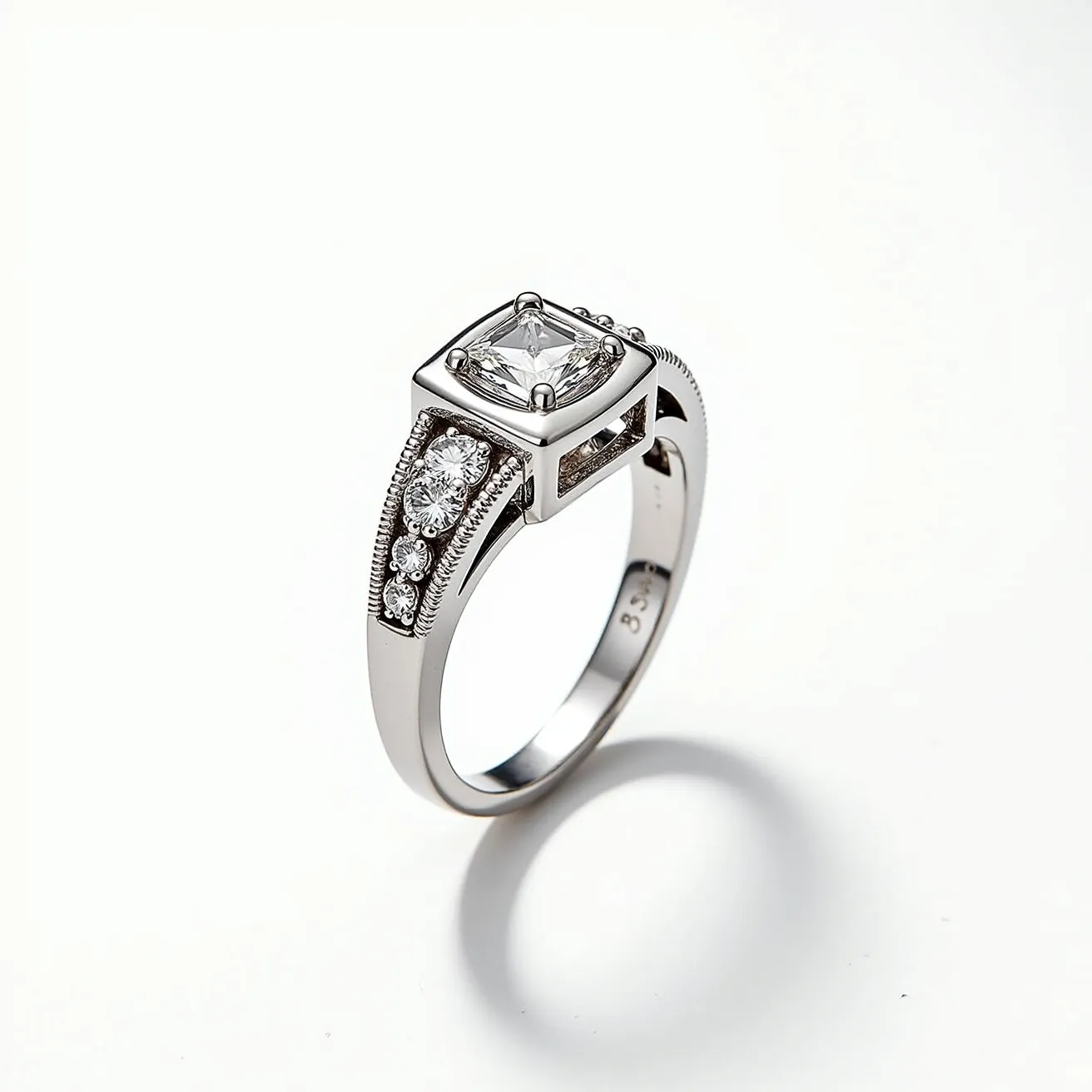 This pinky ring features a sleek metal band, likely made of white gold or platinum, accentuated by a modern and elegant design. At its center, a square-cut diamond is securely set in a prong setting, which adds a stunning focal point to the piece. The band itself is adorned with smaller round diamonds, each set in a pavé style, adding extra sparkle and elegance to the design. The craftsmanship includes a milgrain detail along the edges, enhancing its luxurious appearance. There does not appear to be a visible clasp or adjustment mechanism, indicative of a typical ring band design.