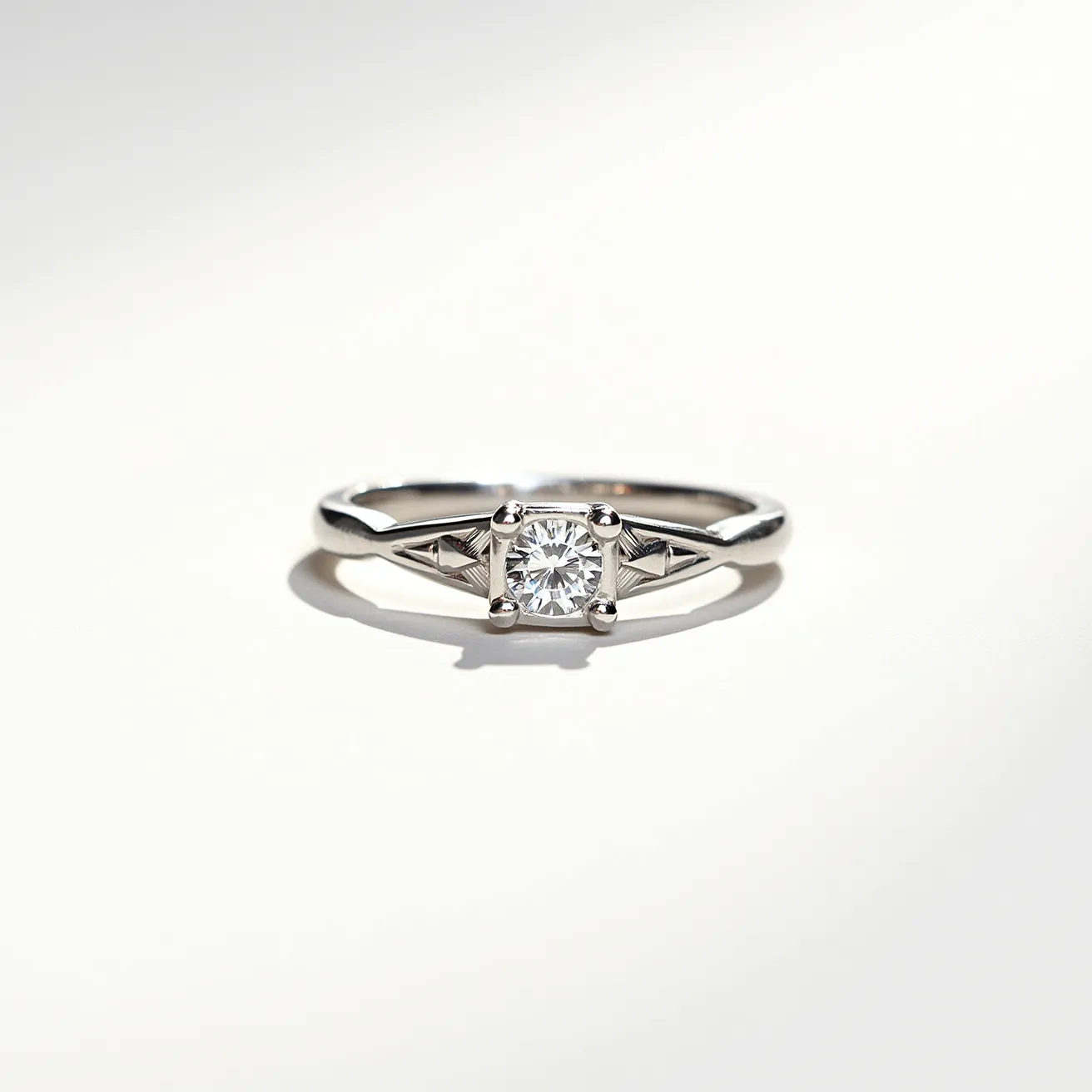 This pinky ring features a sleek metal band, likely made from a polished silver or white gold, exuding a lustrous finish. At its center, a single, round-cut diamond is prominently displayed, secured by a four-prong setting that highlights its brilliance. Flanking the central stone are subtle geometric engravings, adding a touch of elegance to the overall design. The simplicity and elegance of the ring are pronounced by its meticulous craftsmanship and refined aesthetic.