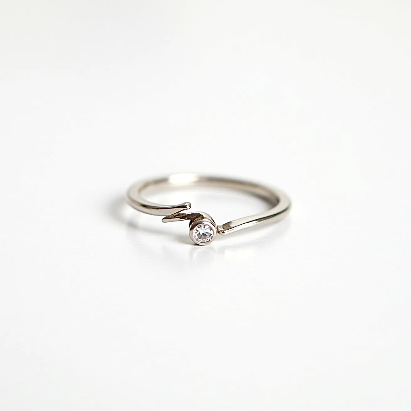 This pinky ring features a sleek and minimalist design, crafted from a polished metal that gives it a smooth and shiny appearance. At the center of the ring is a single, round-cut gemstone, securely held in place by a bezel setting, which enhances its reflective quality and adds a touch of elegance. The open-ended design of the band allows for a comfortable fit, with a unique wrap-around style that adds visual interest and distinction to the piece. The simplicity of the overall form ensures that the gemstone remains the focal point, showcasing its brilliance and clarity. This ring combines functionality with subtle sophistication, making it a stylish accessory for any occasion.