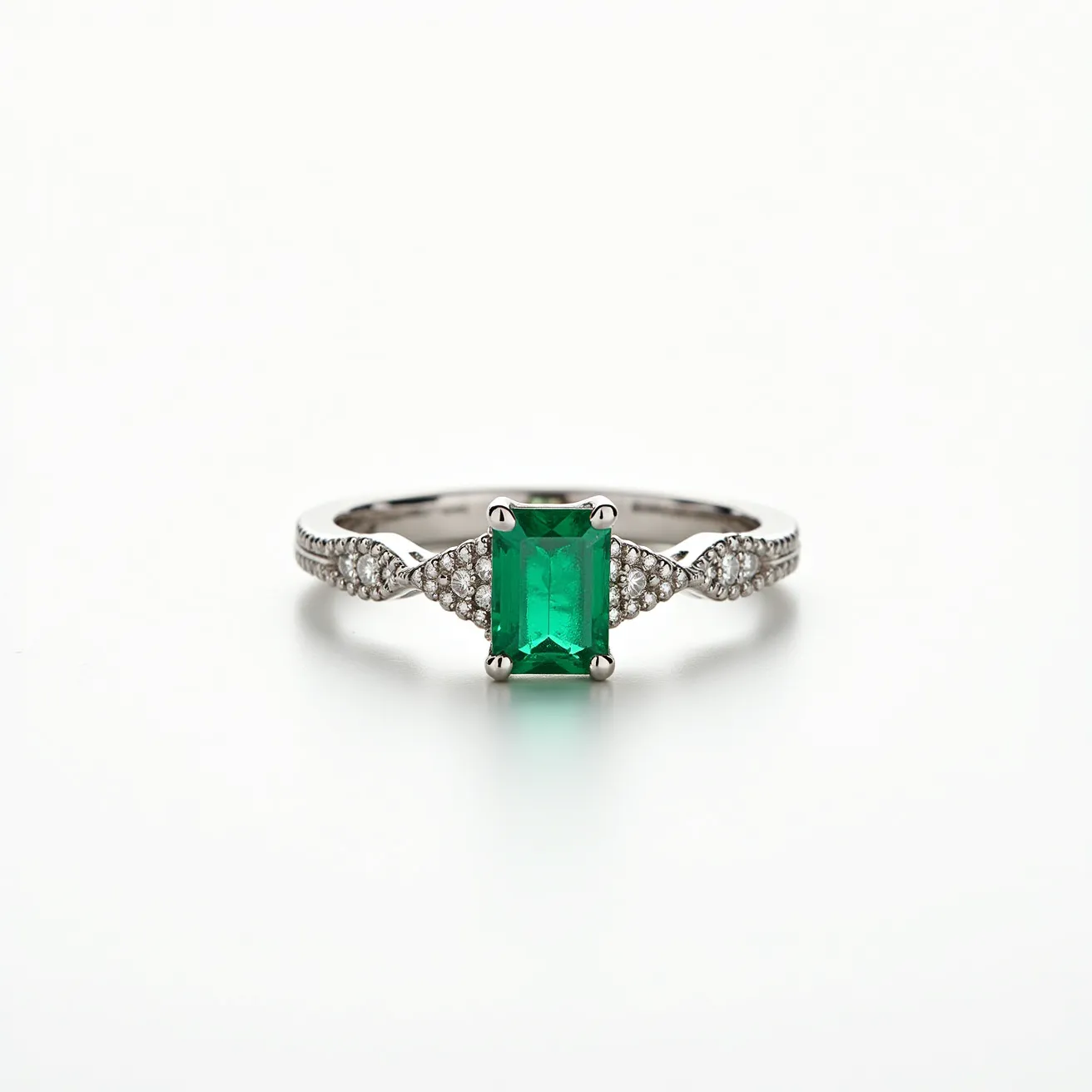 This pinky ring features a stunning emerald-cut green gemstone set centrally, likely an emerald, held securely in place by four prongs. Surrounding the central stone are smaller round brilliant-cut diamonds embedded in the band, which add a sparkling accent to the overall design. The band itself appears to be crafted from a polished white metal, possibly white gold or platinum, enhancing the elegance of the ring. The combination of the vibrant center stone with the shimmering diamonds creates a striking and luxurious appearance.