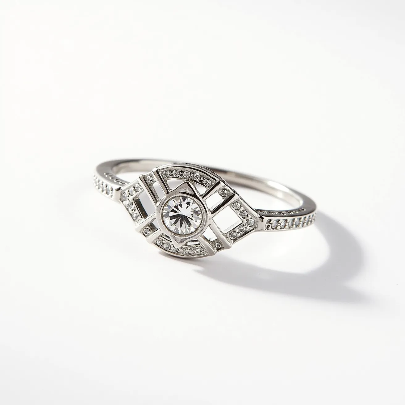 This promise ring features an elegant combination of white metal, likely silver or white gold, and a stunning central gem set in a distinctive geometric design. The central stone appears to be a round-cut diamond or diamond-like gem, set securely in a bezel setting, surrounded by a series of smaller round-cut stones that are elegant and complementary. These smaller stones are meticulously arranged in a geometric pattern, enhancing the ring's sophisticated appearance. The band is adorned with additional small round stones, adding a touch of sparkle. The overall design is sleek and modern, with no additional clasps or attachments, offering a seamless and elegant look.