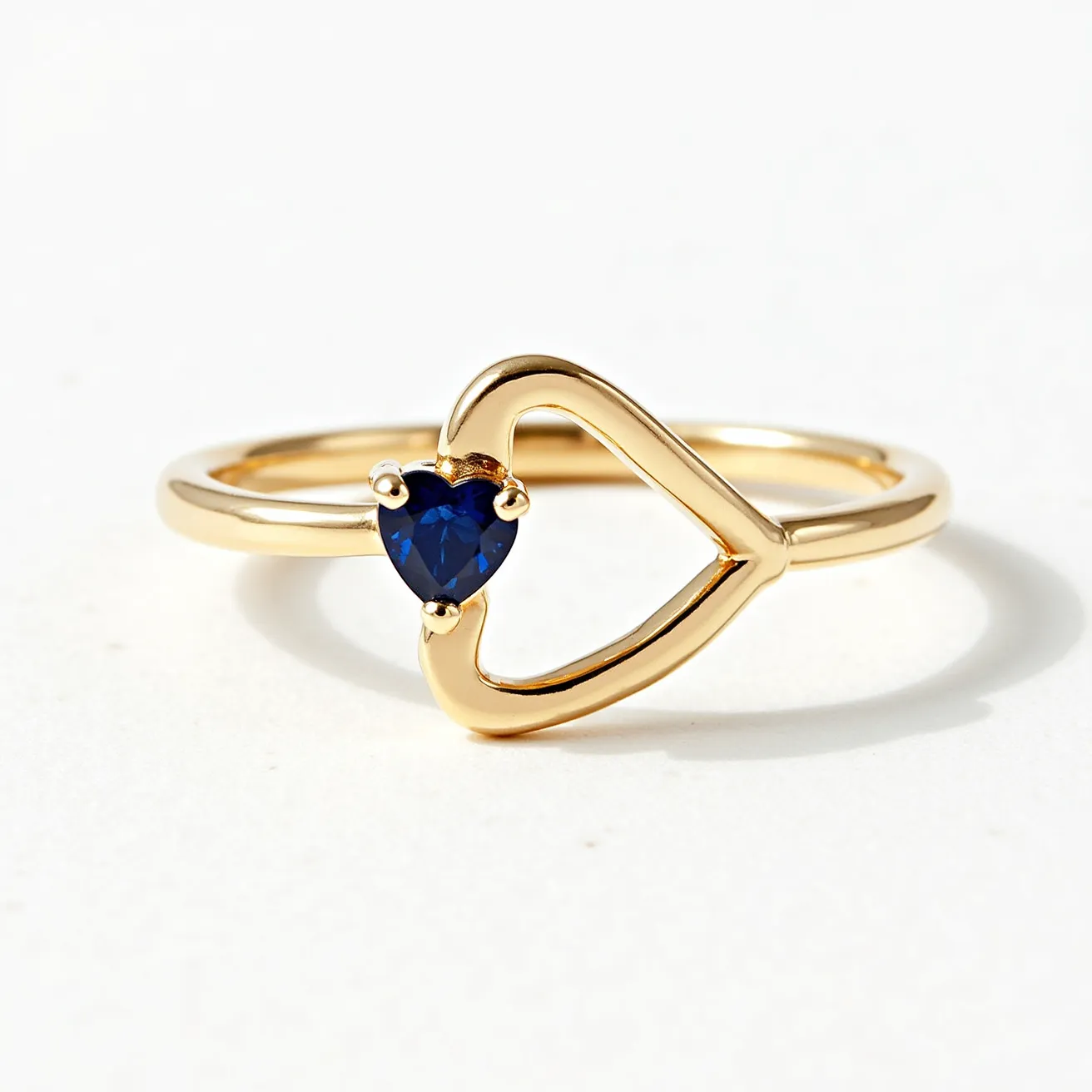 This promise ring features a delicate gold band that gracefully forms an open heart shape. At the center of the heart is a heart-cut blue sapphire, secured by three prongs, adding a vibrant and romantic touch. The simple yet elegant design is perfect for symbolizing commitment and affection.