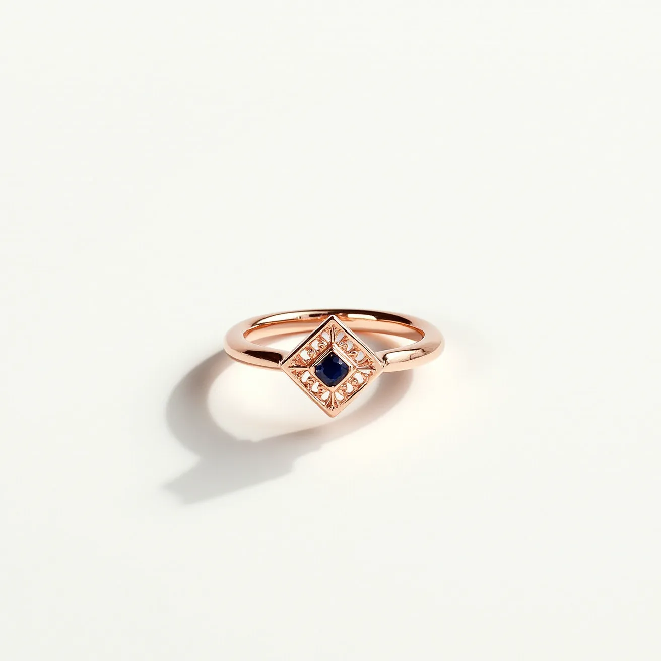 This promise ring features a rose gold band that elegantly supports a diamond-shaped setting. At the center lies a small, dark blue gemstone, likely a sapphire, cut in a round shape and securely set with a bezel setting. Surrounding the central stone are several small, clear gems, adding a touch of sparkle and enhancing the sophisticated design. The simplicity and elegance of the materials and arrangement highlight the ring's symbolism of commitment and love.