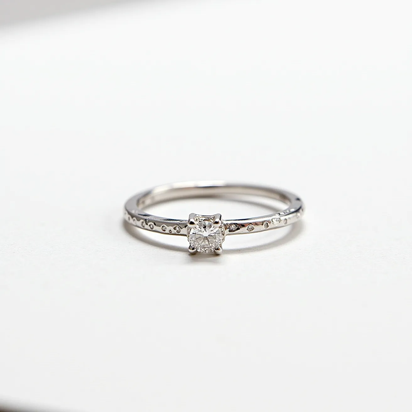 This promise ring features a delicate band crafted from a silver-toned metal, offering a sleek and polished appearance. Set with a sparkling gemstone at its center, the ring showcases a round-cut stone that is prominently displayed in a prong setting, enhancing its brilliance. Along the band, smaller embedded stones add a touch of elegance and sparkle, complementing the central gem. The overall design is minimalist yet elegant, making it a classic symbol of commitment.