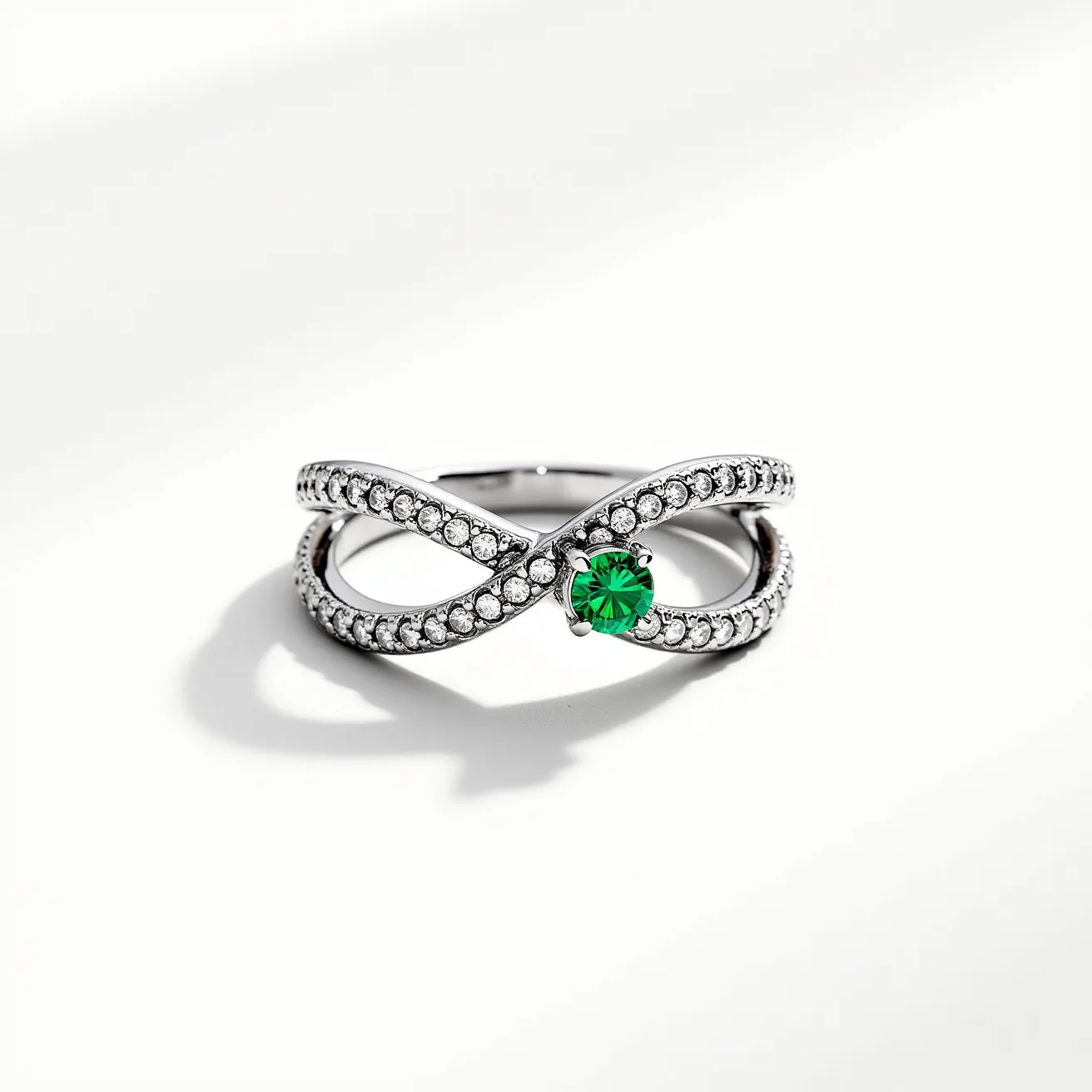 This promise ring features an elegant infinity design made from shiny silver-toned metal, likely sterling silver or white gold. The band is intricately adorned with small, round-cut clear stones, possibly diamonds or cubic zirconia, set in a pavé style that adds a continuous sparkle across its surface. At the center of the design lies a striking round-cut green gemstone, such as an emerald or a green cubic zirconia, held securely in place by a classic prong setting. This combination of materials and design elements creates a symbol of eternity and devotion, making it a fitting promise ring.